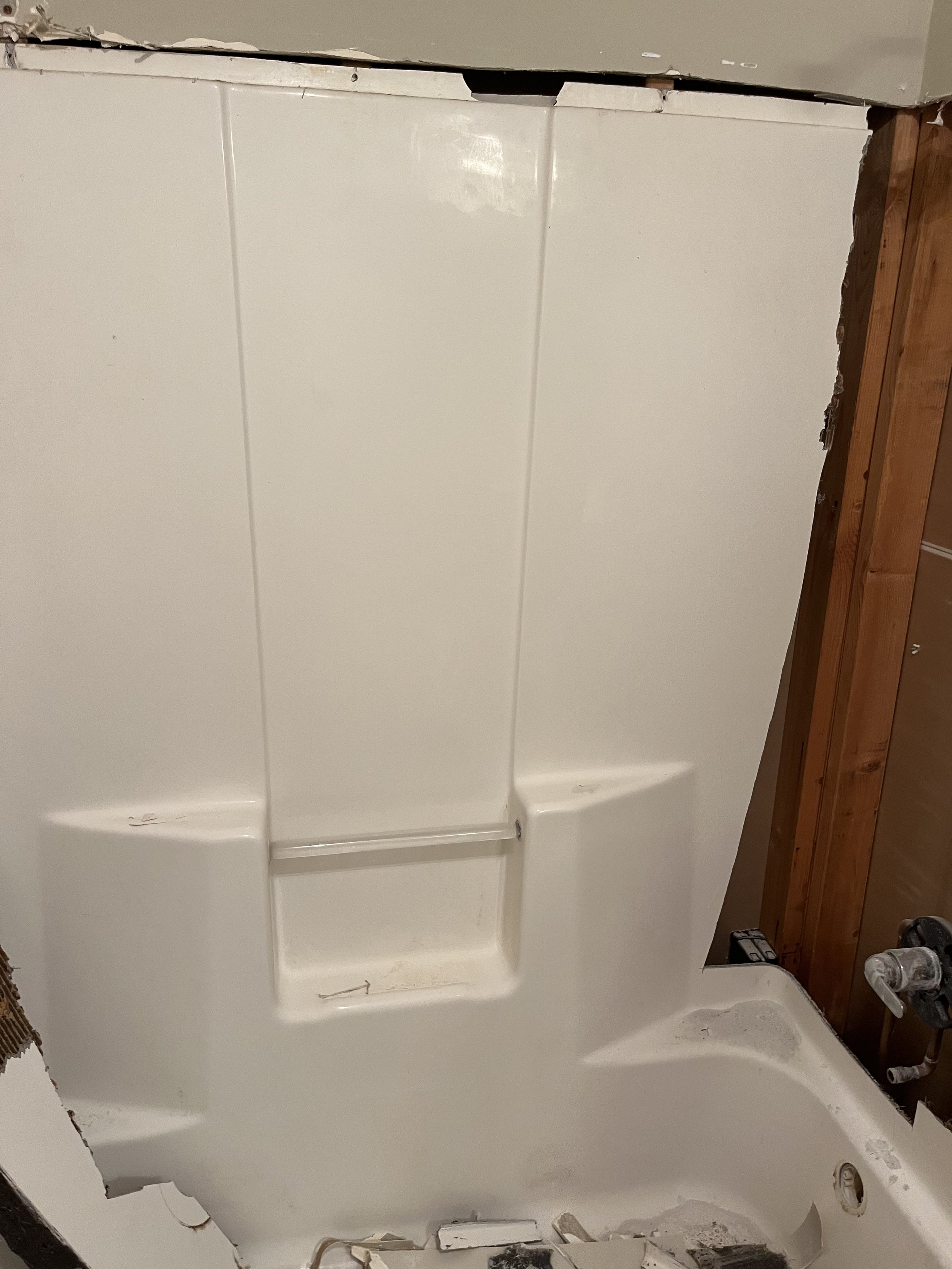 Bathroom shower with white enclosure and some damage on the top edge, dark brown wooden paneling on the wall, and visible plumbing fixtures.