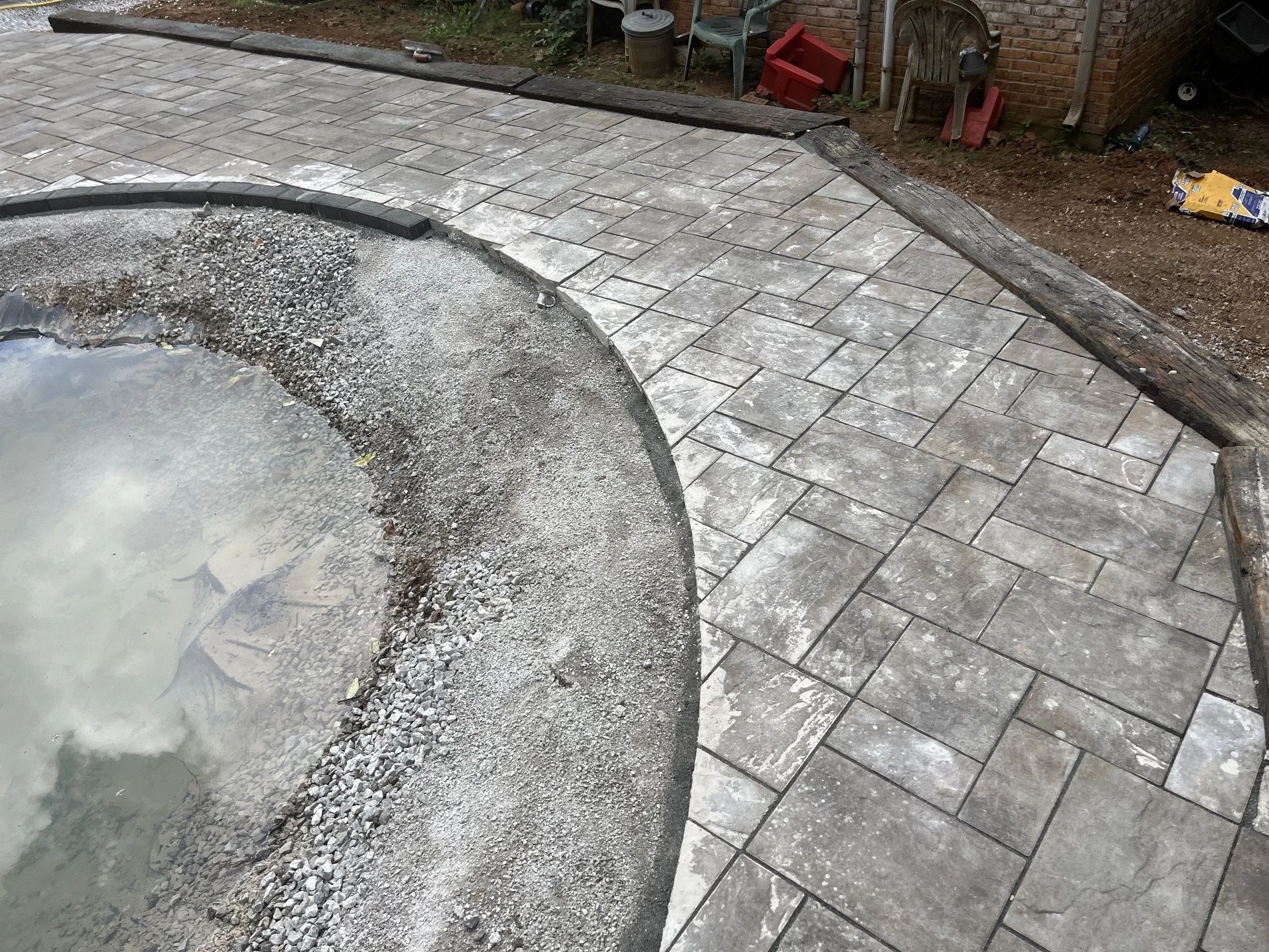 A newly paved stone patio or walkway next to a hot tub, with tools and construction materials around, early in the installation process.