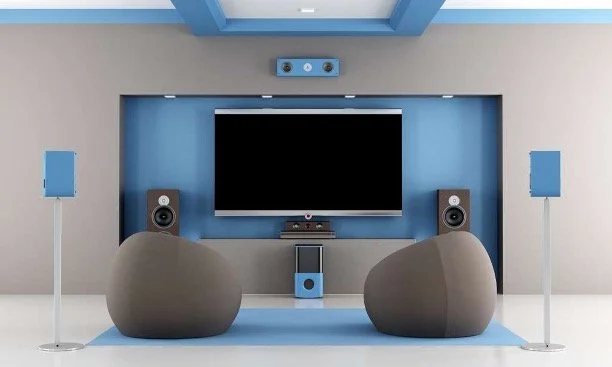 Modern home theater room with a large flat-screen TV, two gray bean bag chairs, two blue speakers, and a blue and gray color scheme.