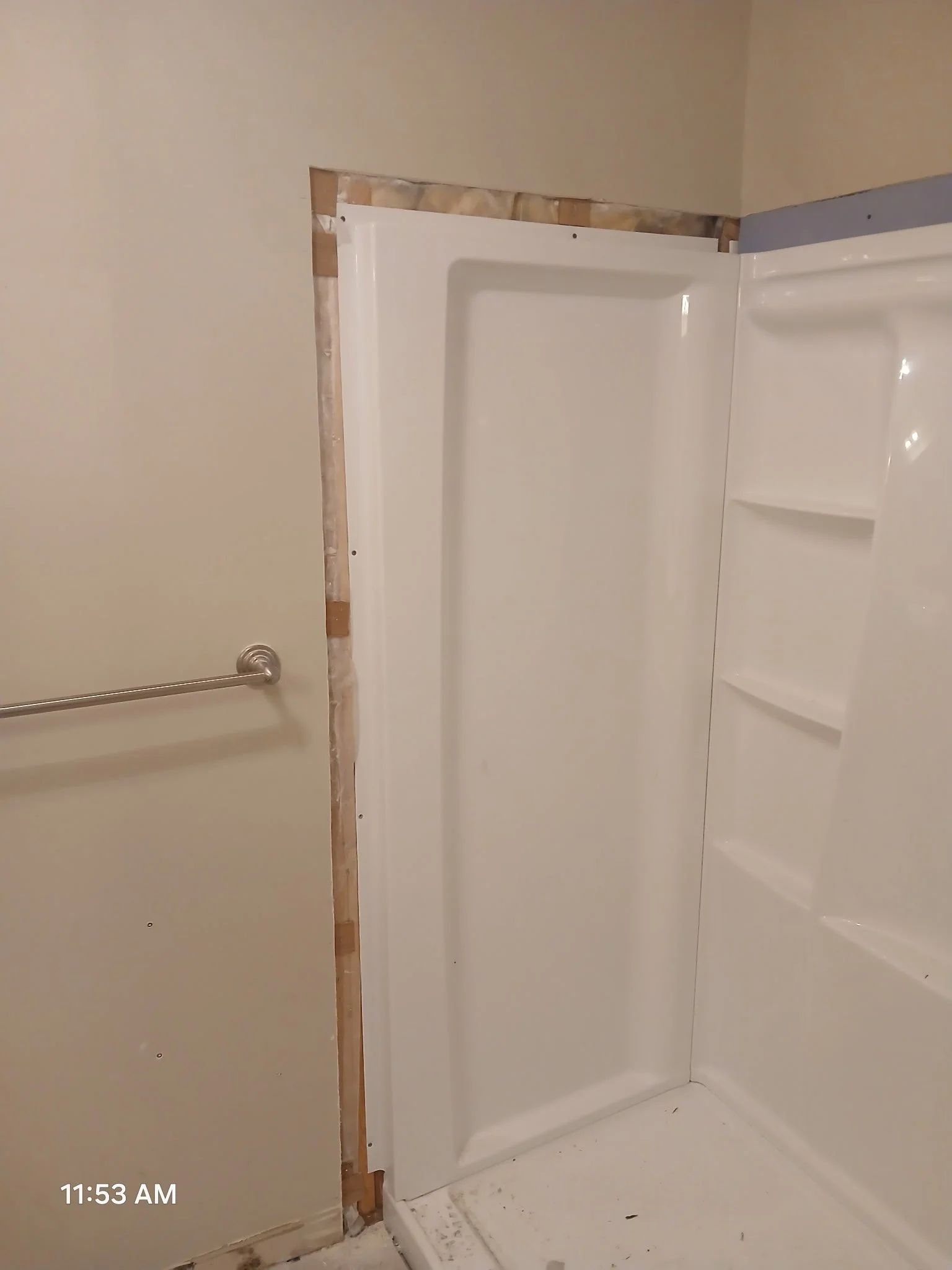 A shower stall installed in a bathroom with exposed wall framing around it.