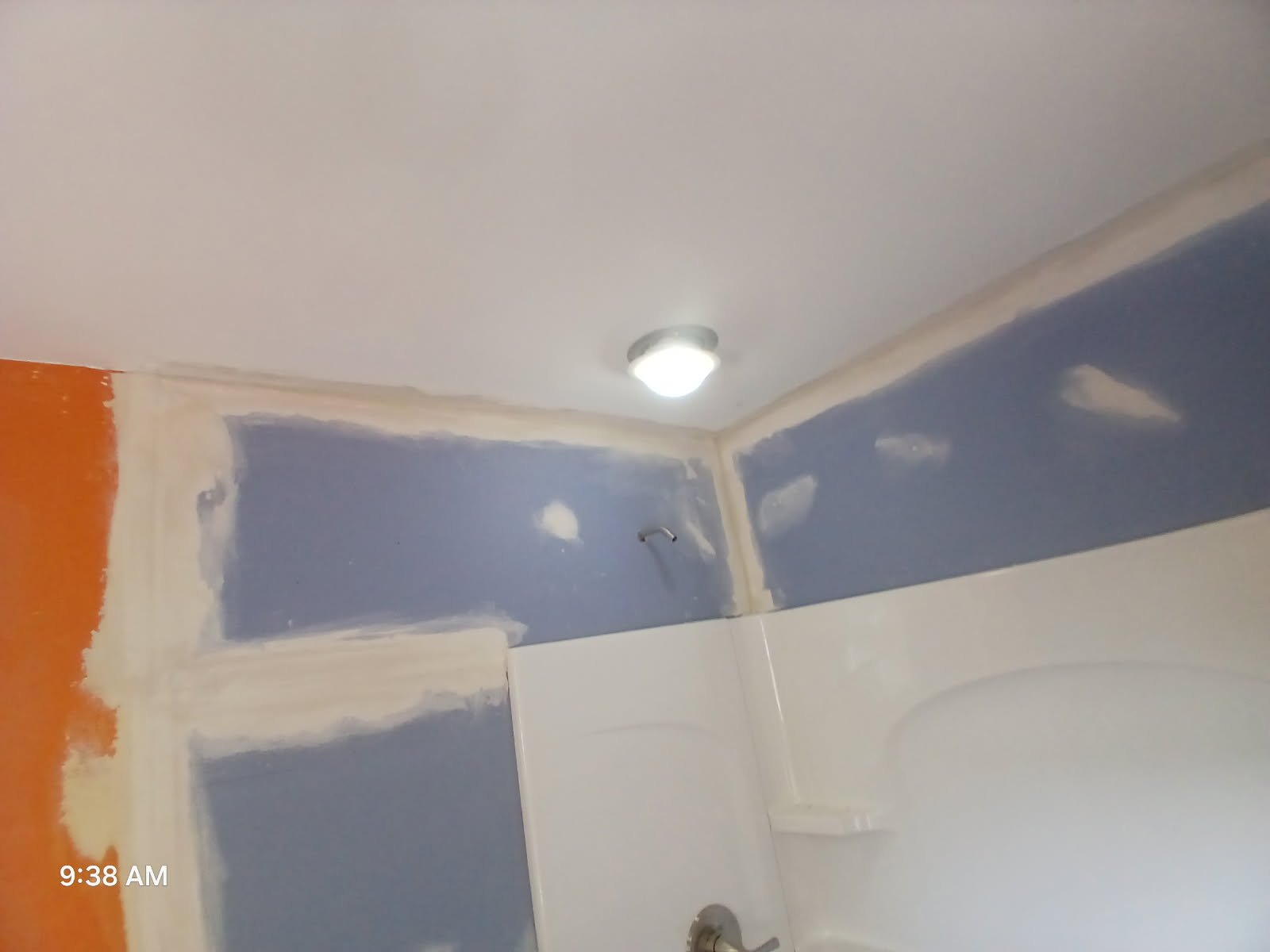 Bathroom ceiling being painted blue with patching at the corners and a ceiling light fixture on