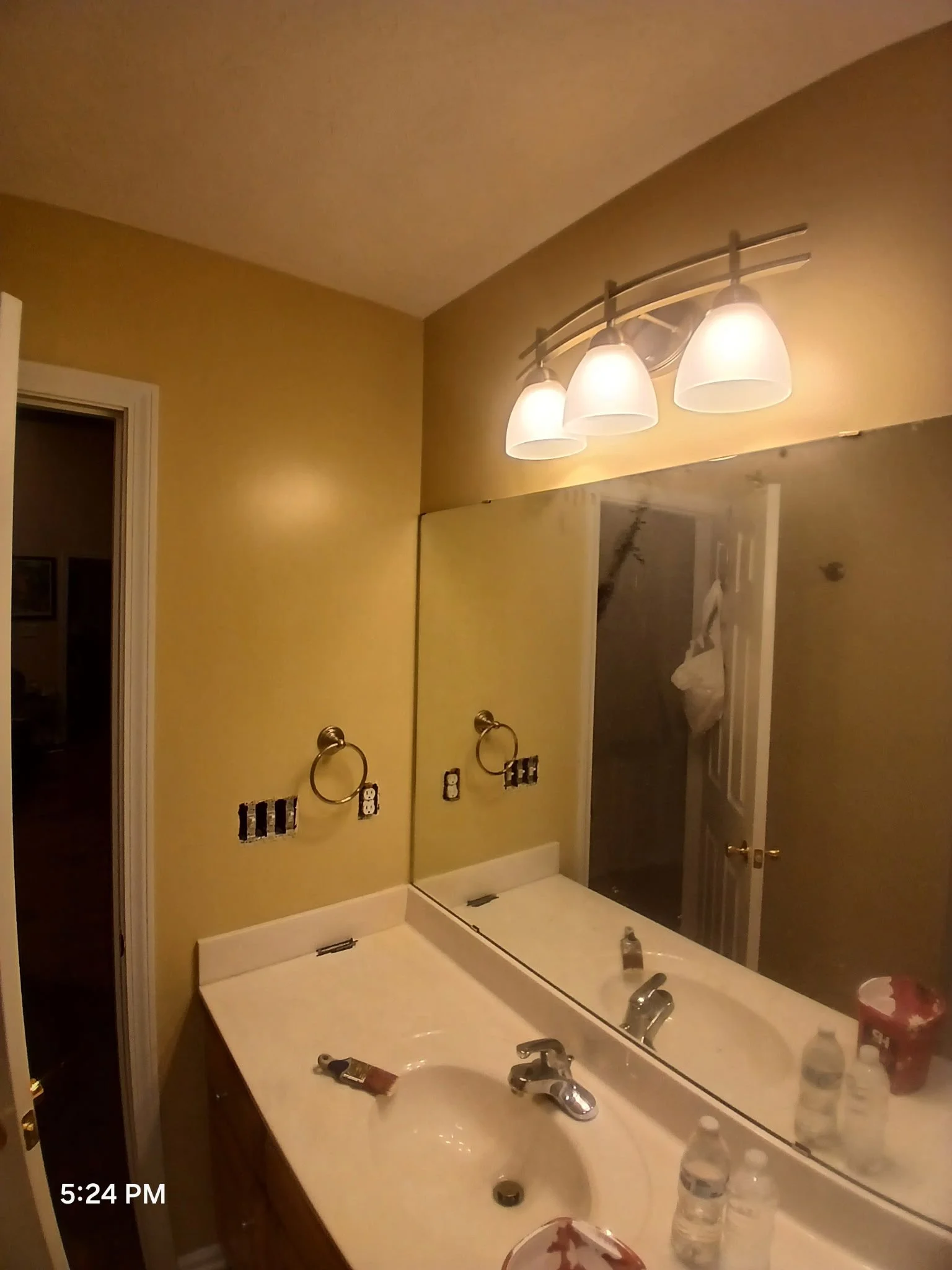 Bathroom mirror above sink with toiletries and a light fixture with three bulbs.