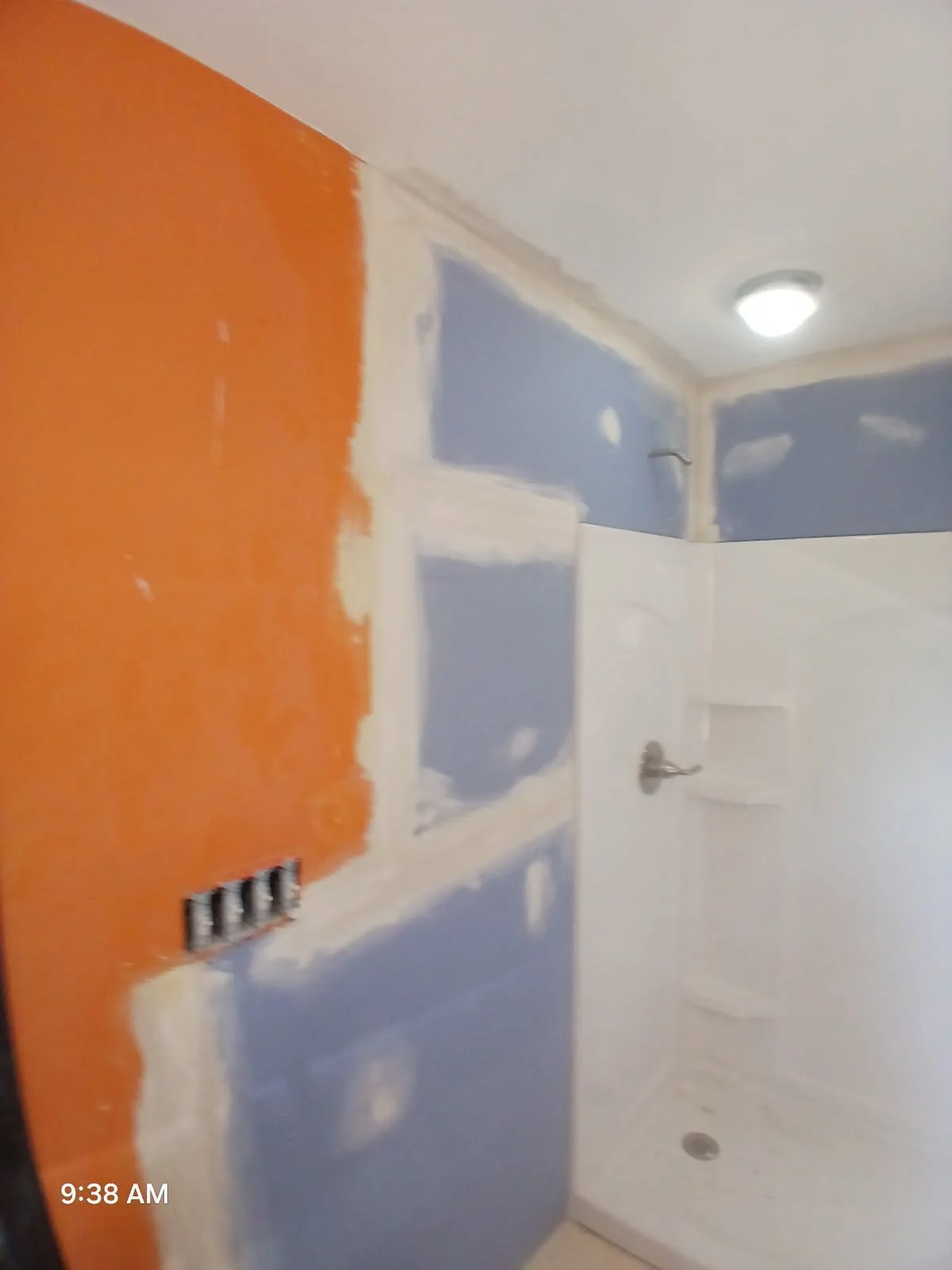Bathroom under renovation with partly painted walls in blue, white, and orange, with drywall mud, electrical outlets, and a shower area.
