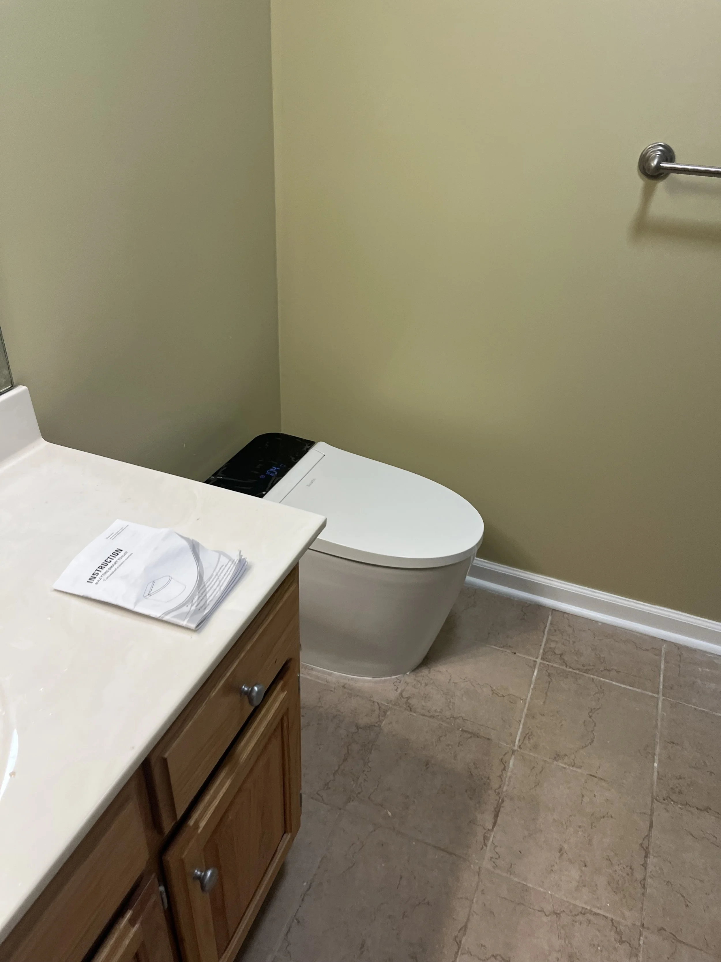 Bathroom with a modern toilet, a wooden cabinet with a countertop, and a towel rack on the wall.