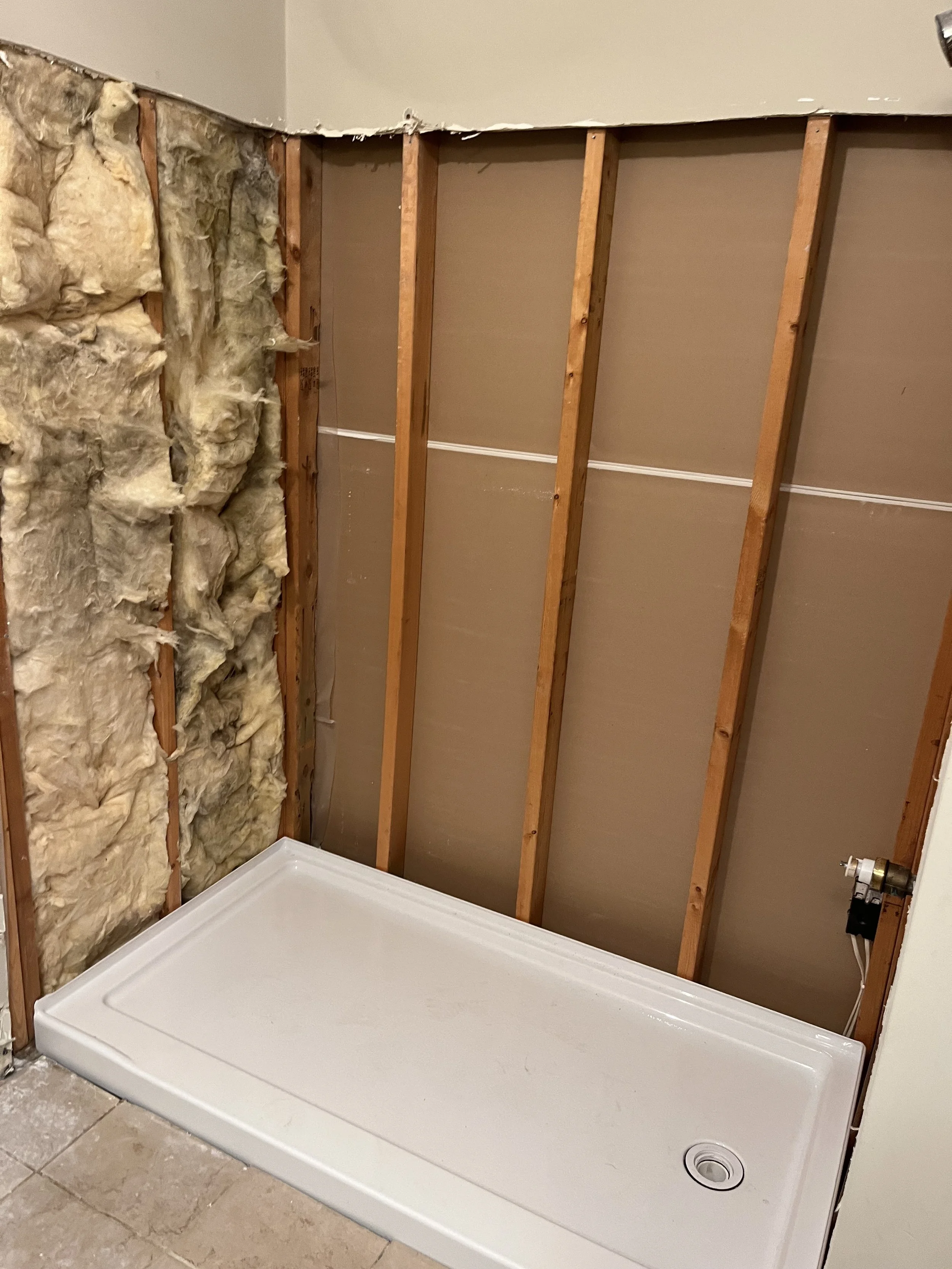 Bathroom renovation with exposed wall studs, insulation, and a new shower base installed