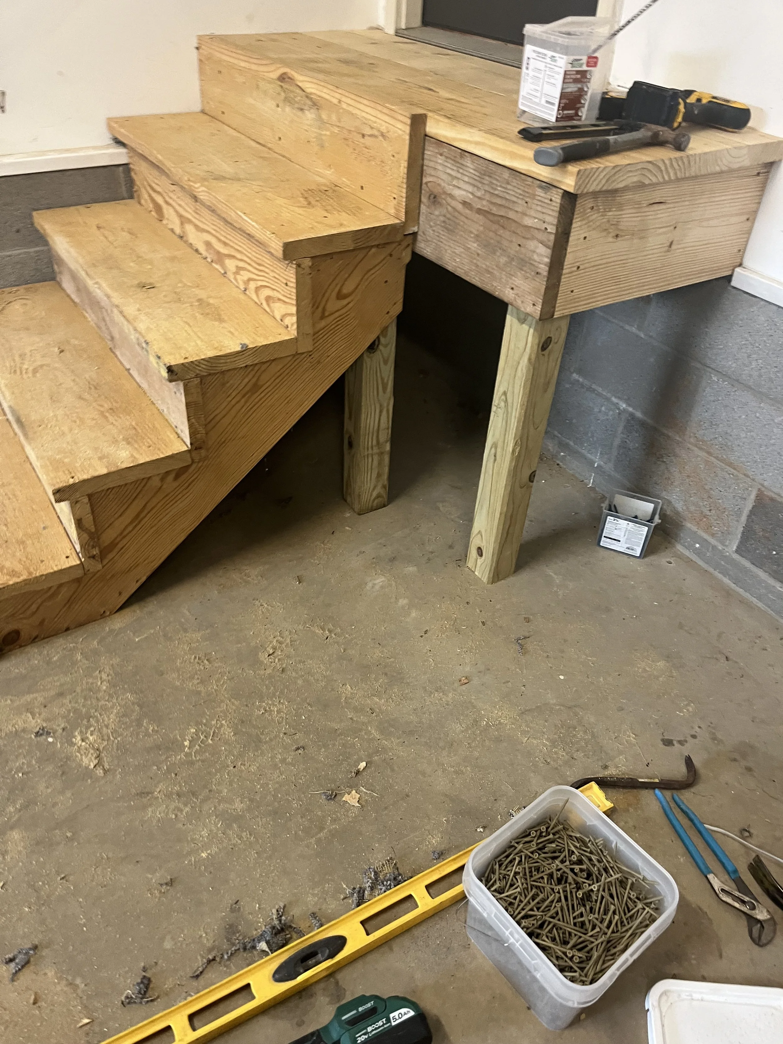 Wooden stairs and workbench in a workshop with tools and screws on the floor.