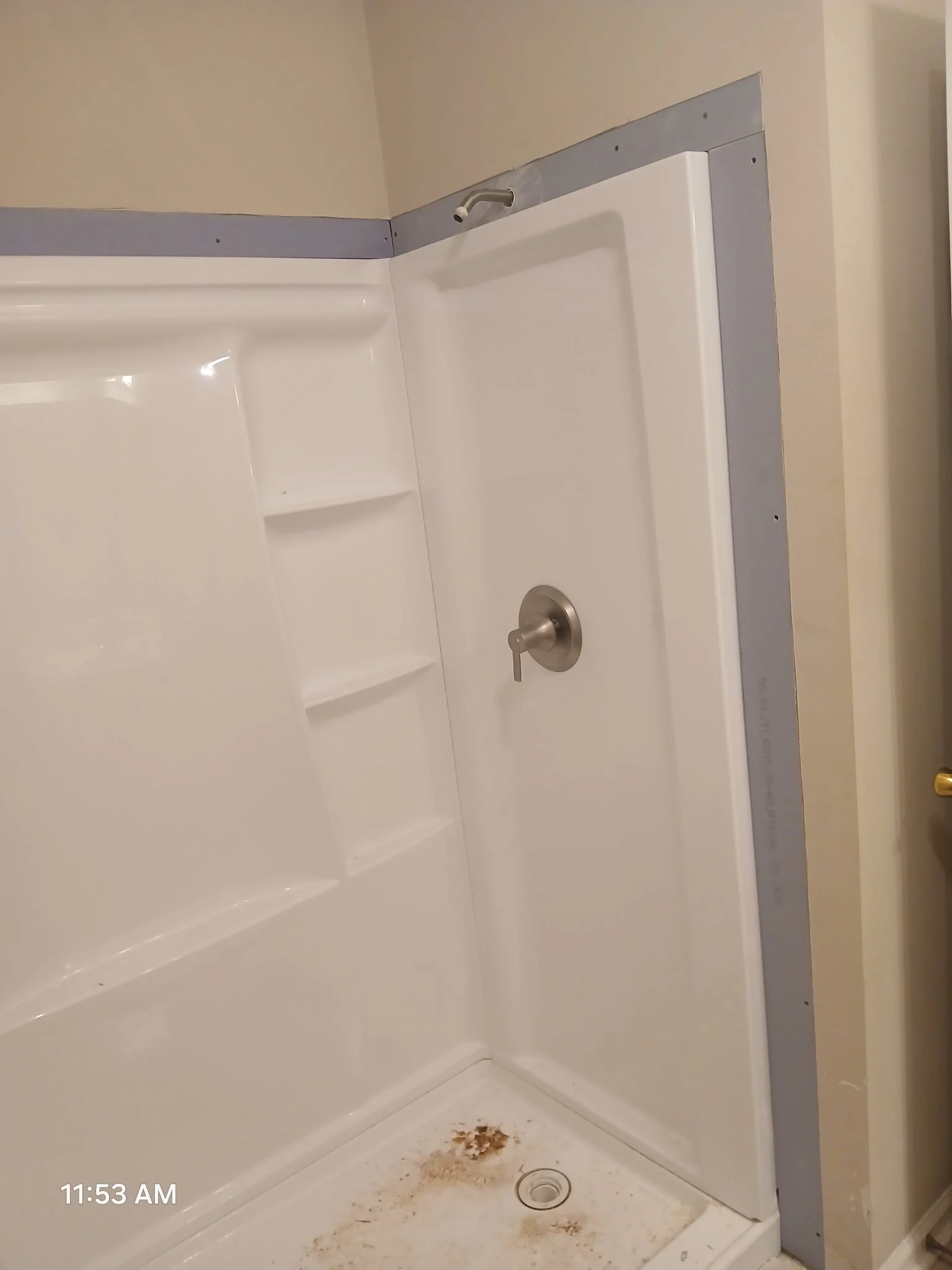 Photo of an empty bathtub shower with a spray handle, metal faucet, and small amount of dirt or rust stains at the bottom of the shower stall.