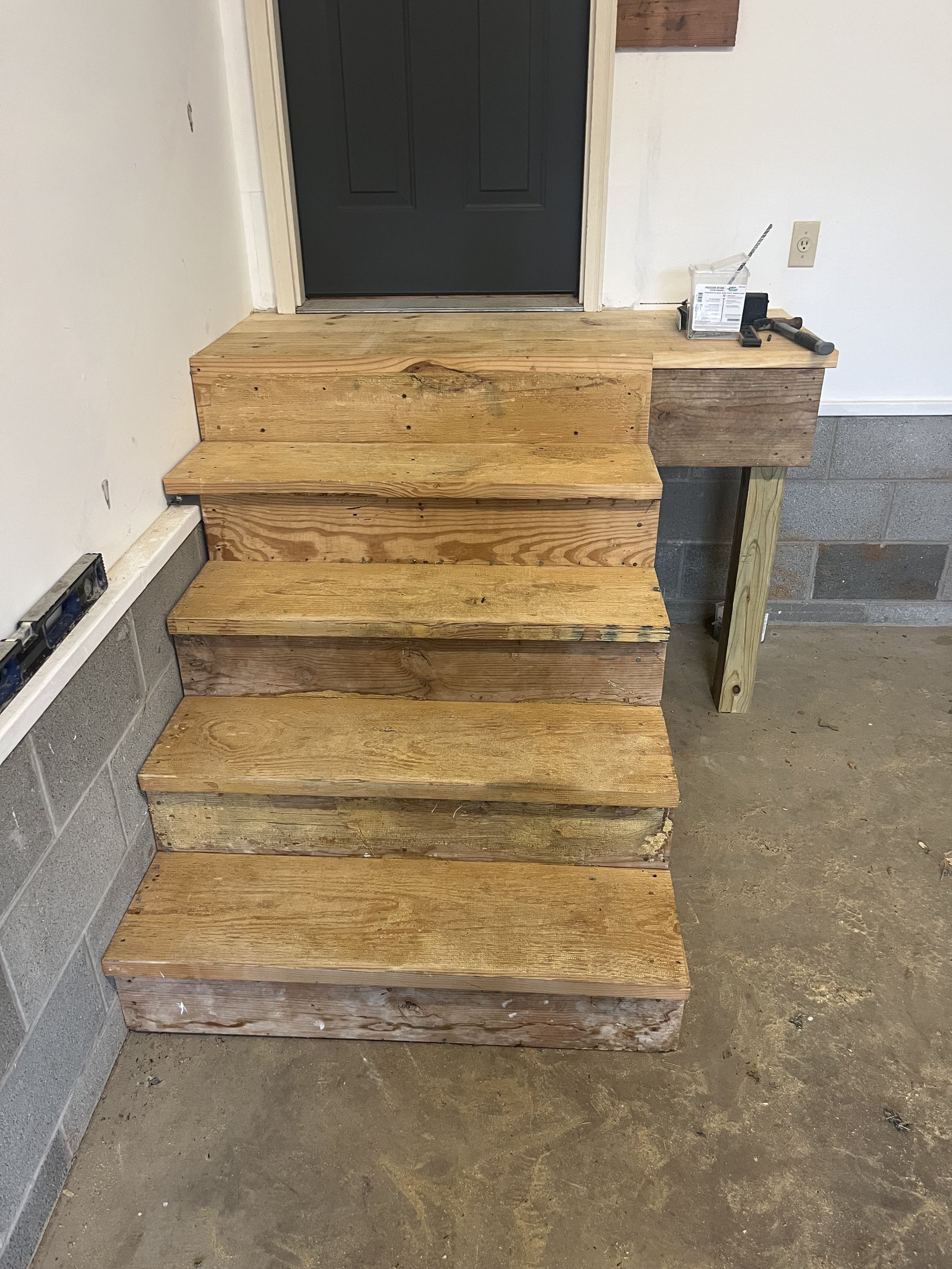 Wooden stairs leading up to a door with a dark gray finish in a construction or renovation site.