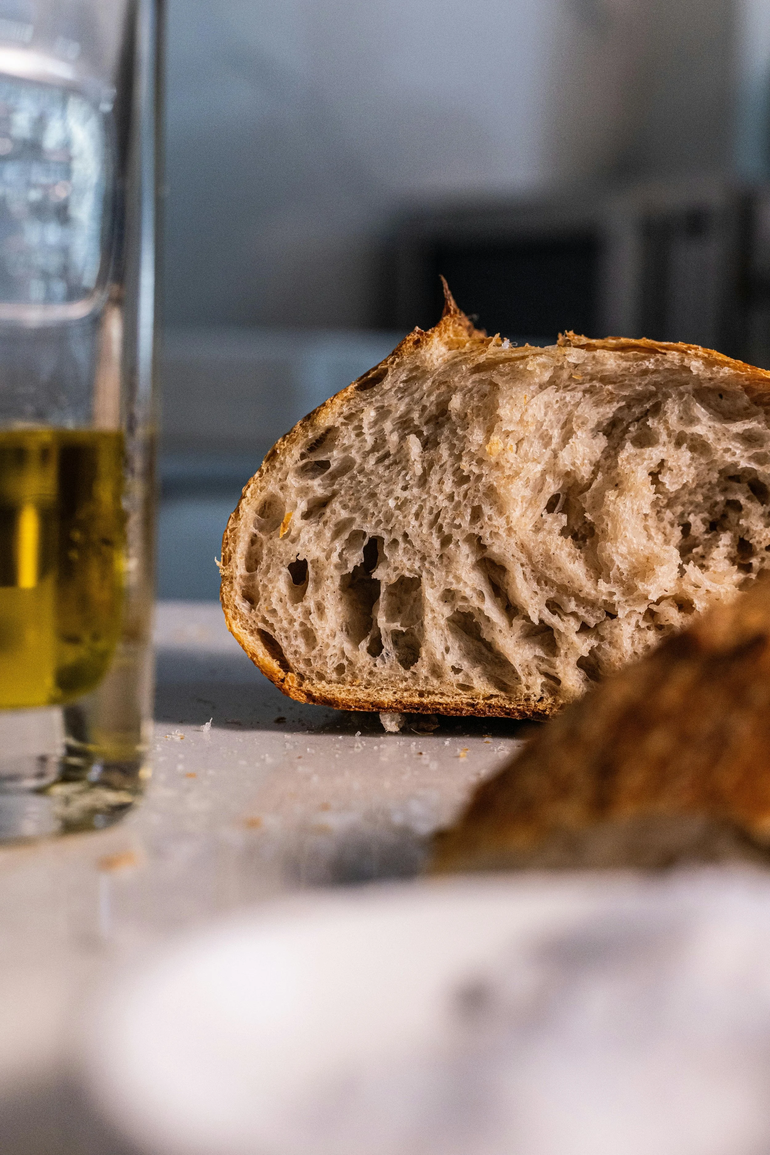 Close-up of a sliced loaf of rustic bread on a kitchen counter with a glass of olive oil nearby.