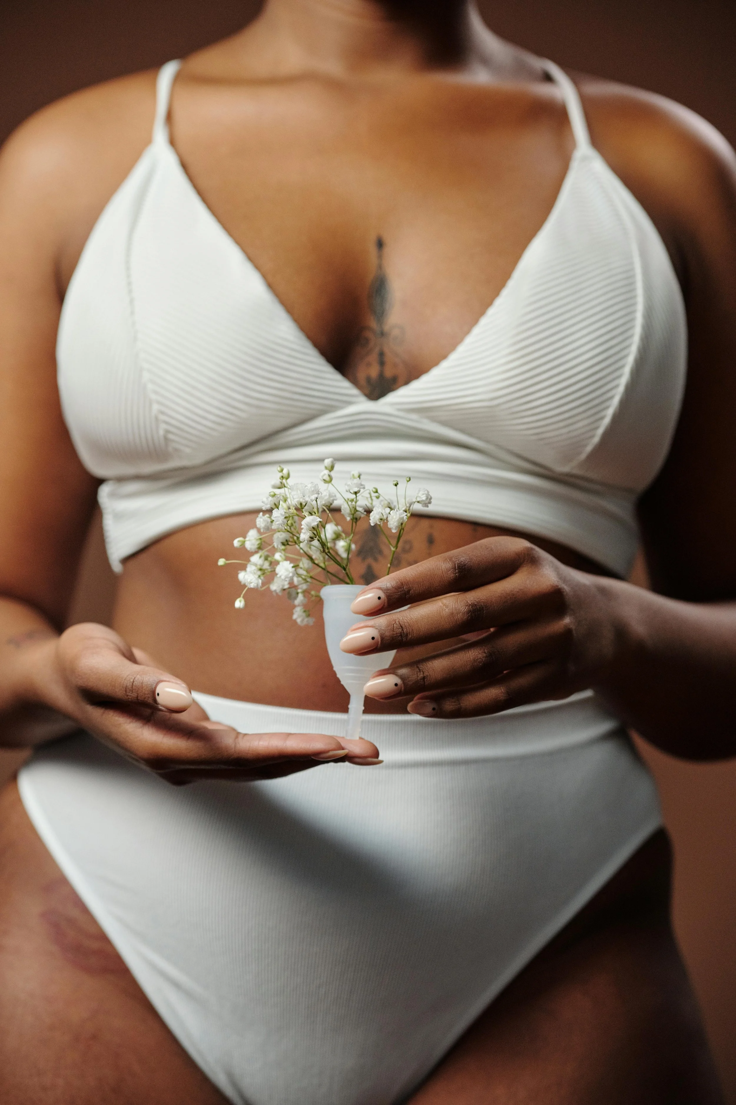 A woman in white lingerie holding a menstrual cup with white flowers.