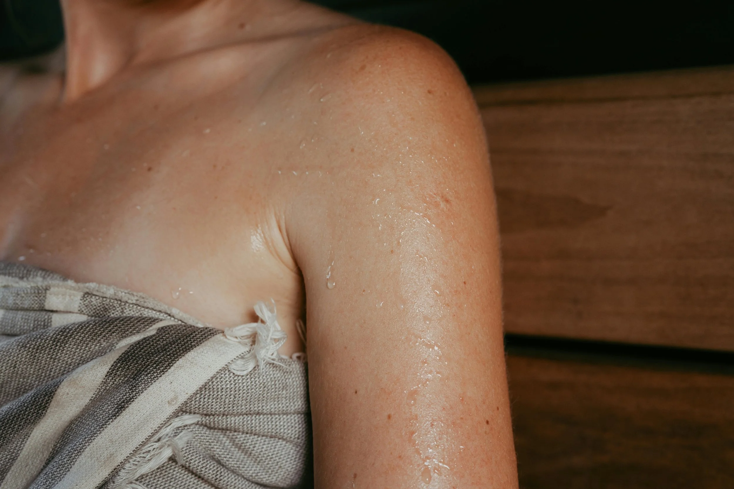 Close-up of a person's shoulder and upper arm with water droplets on skin, leaning against a wooden surface.