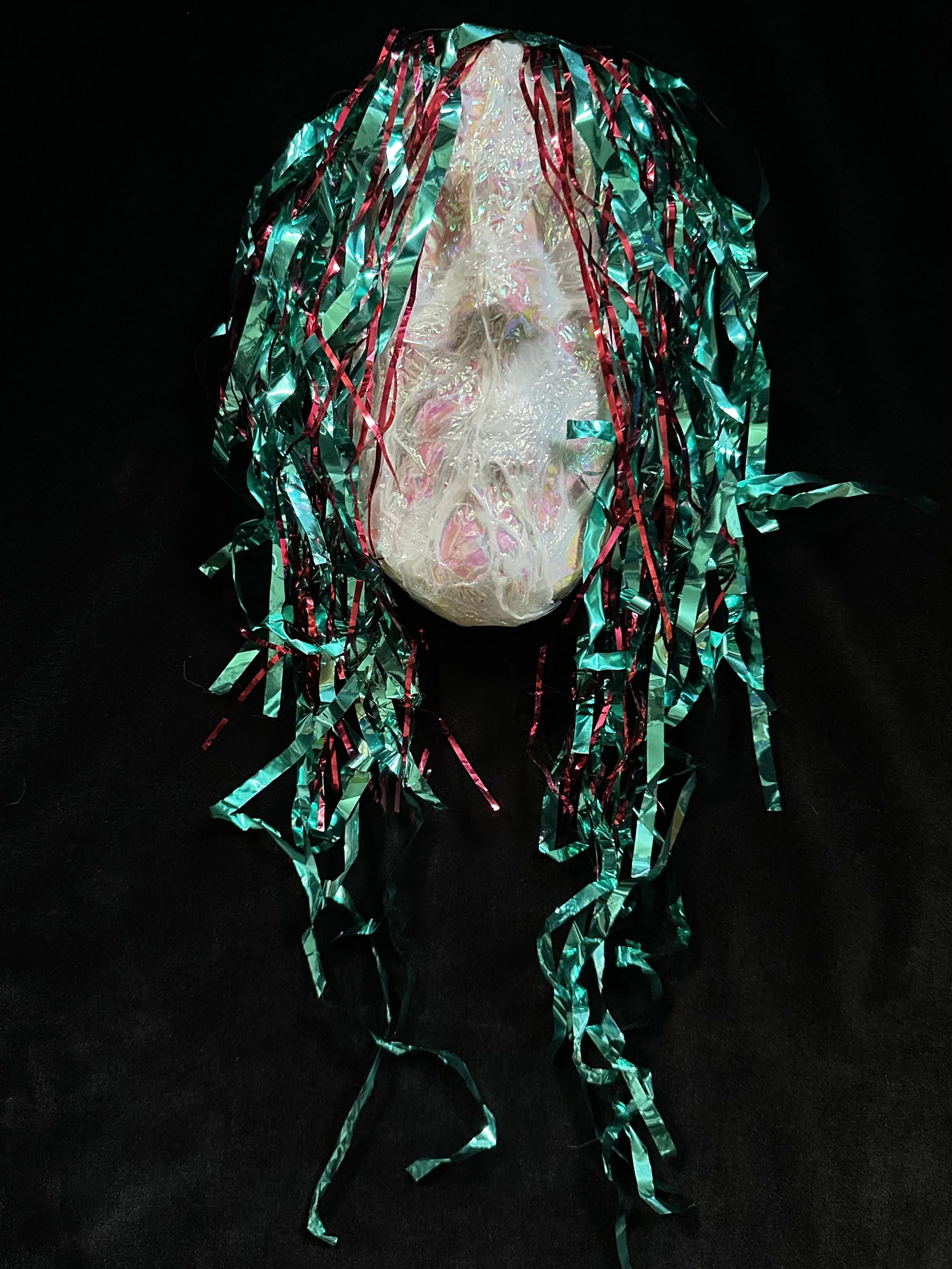"Reveler", Laura Nelsen, papier-mâché clay, iridescent shrink film, mylar streamers and acrylic paint, 20"x6"x3.5", 2026.