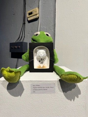"Rory Shrine", Laura Nelsen, papier-mâché clay, ink paw print, whiskers, tuft of Rory's fur, Kermit stuffed toy and acrylic paint. 2026