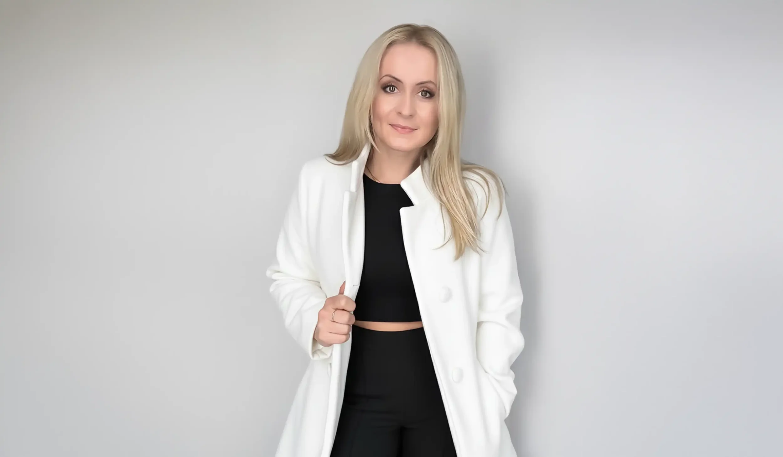 Aliona Bonano, a professional Saint Louis-based graphic designer, wearing a modern white coat and black attire, posing against a clean gray background in a high-end studio portrait.
