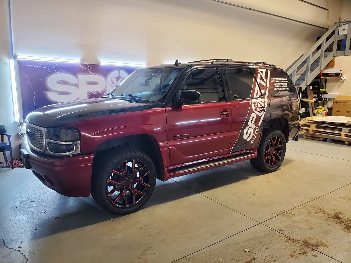 Red SUV with black hood and custom black and red rims in workshop with a SP Auto Protect decal on the side and a purple SP logo with lightning in the background.