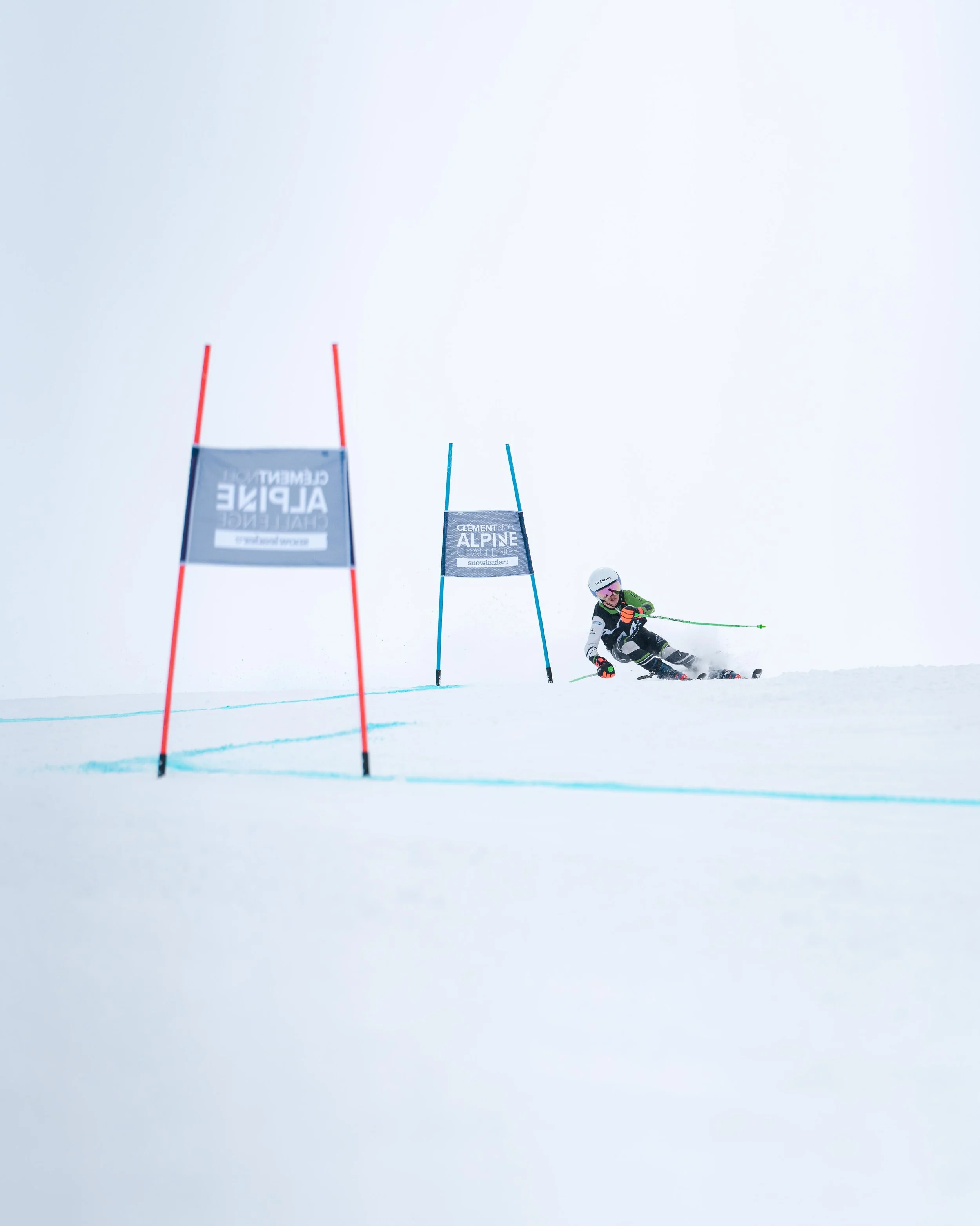 Skieur en course de slalom alpin sur une piste enneigée avec des portes de slalom et fond blanc.