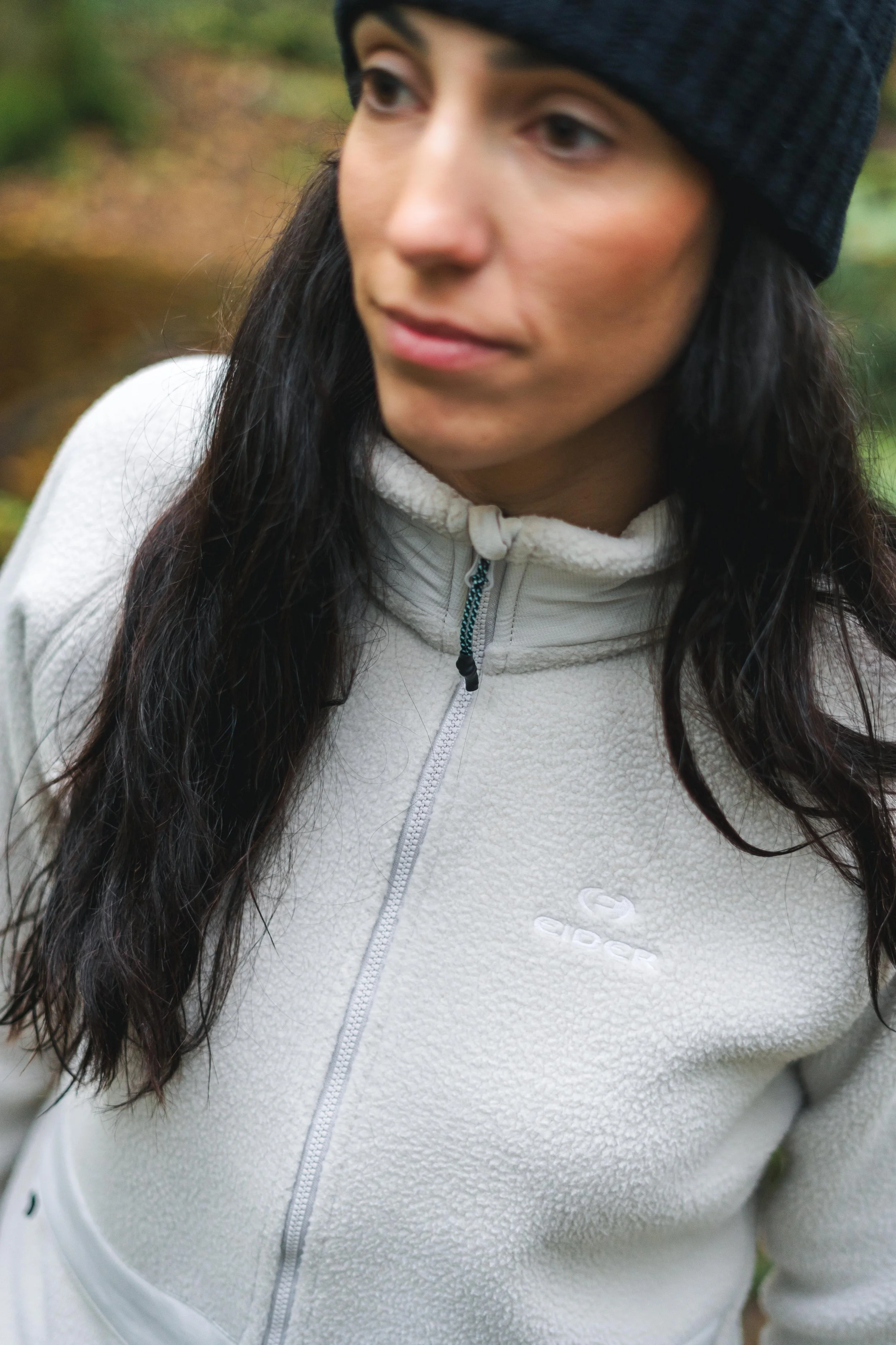 Femme portant une veste en polaire blanche et un bonnet noir, en extérieur.