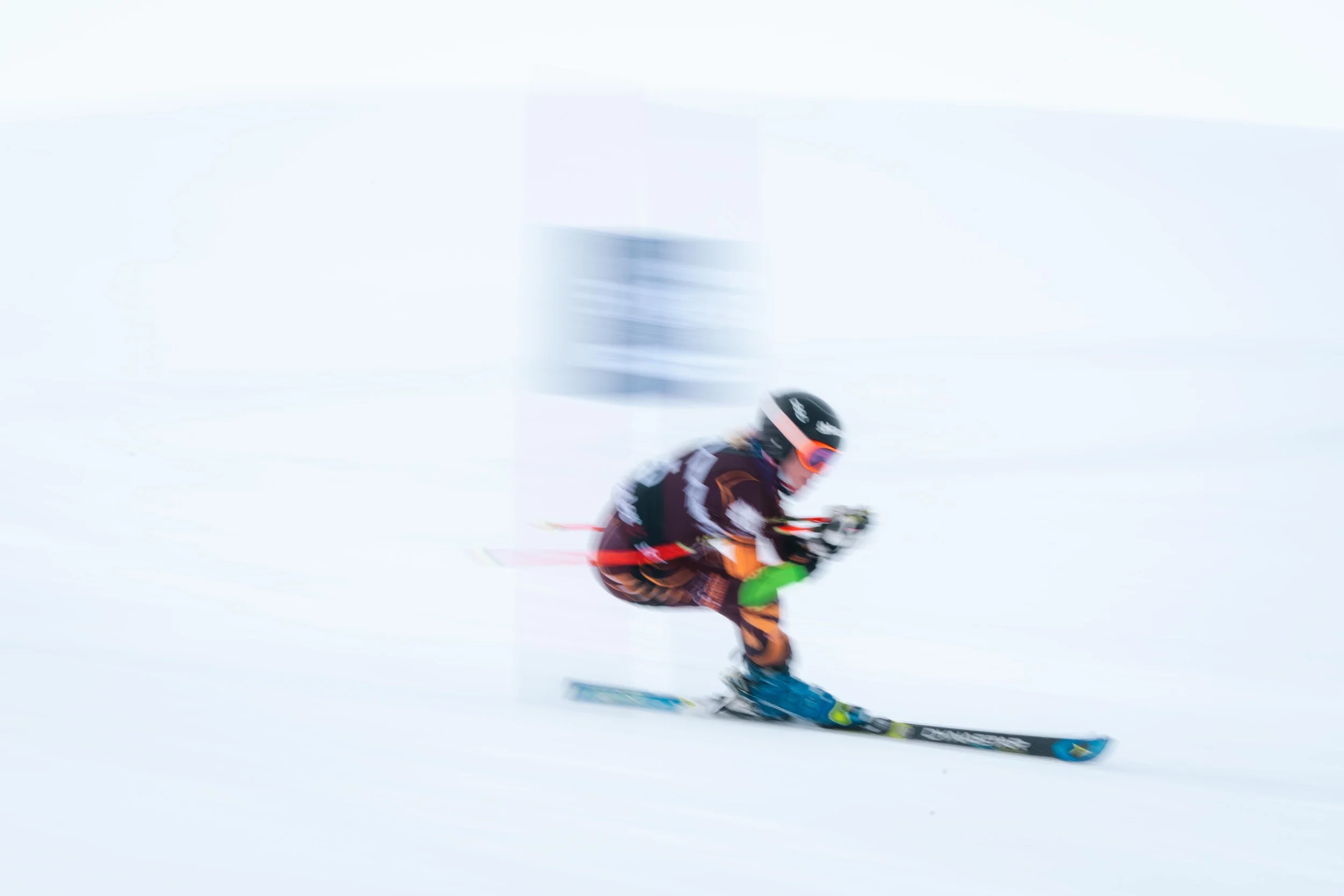 Skieur en mouvement rapide sur une piste enneigée, avec équipement de ski et combinaison colorée, un fond flou indiquant la vitesse.