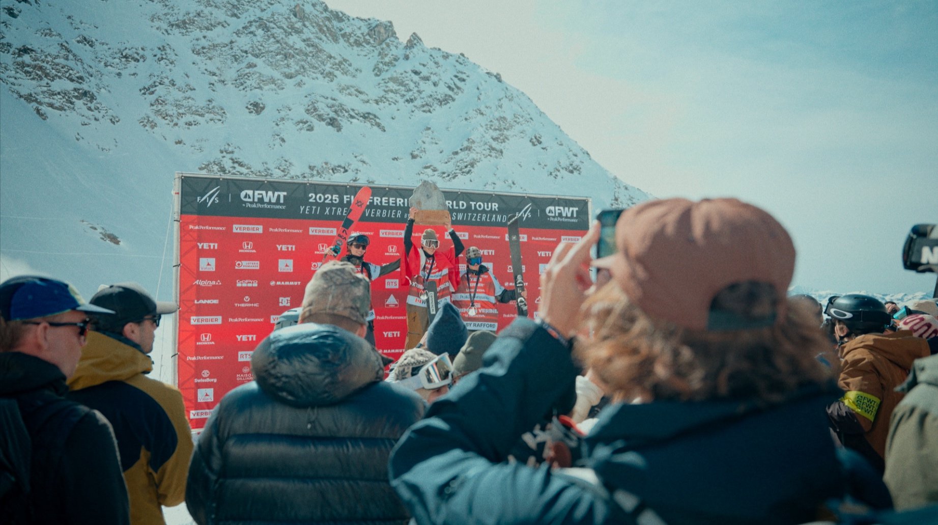 Cérémonie de remise des prix au Freeride World Tour 2025 à Verbier, Suisse, avec des skieurs sur un podium, des spectateurs et des montagnes enneigées en arrière-plan.