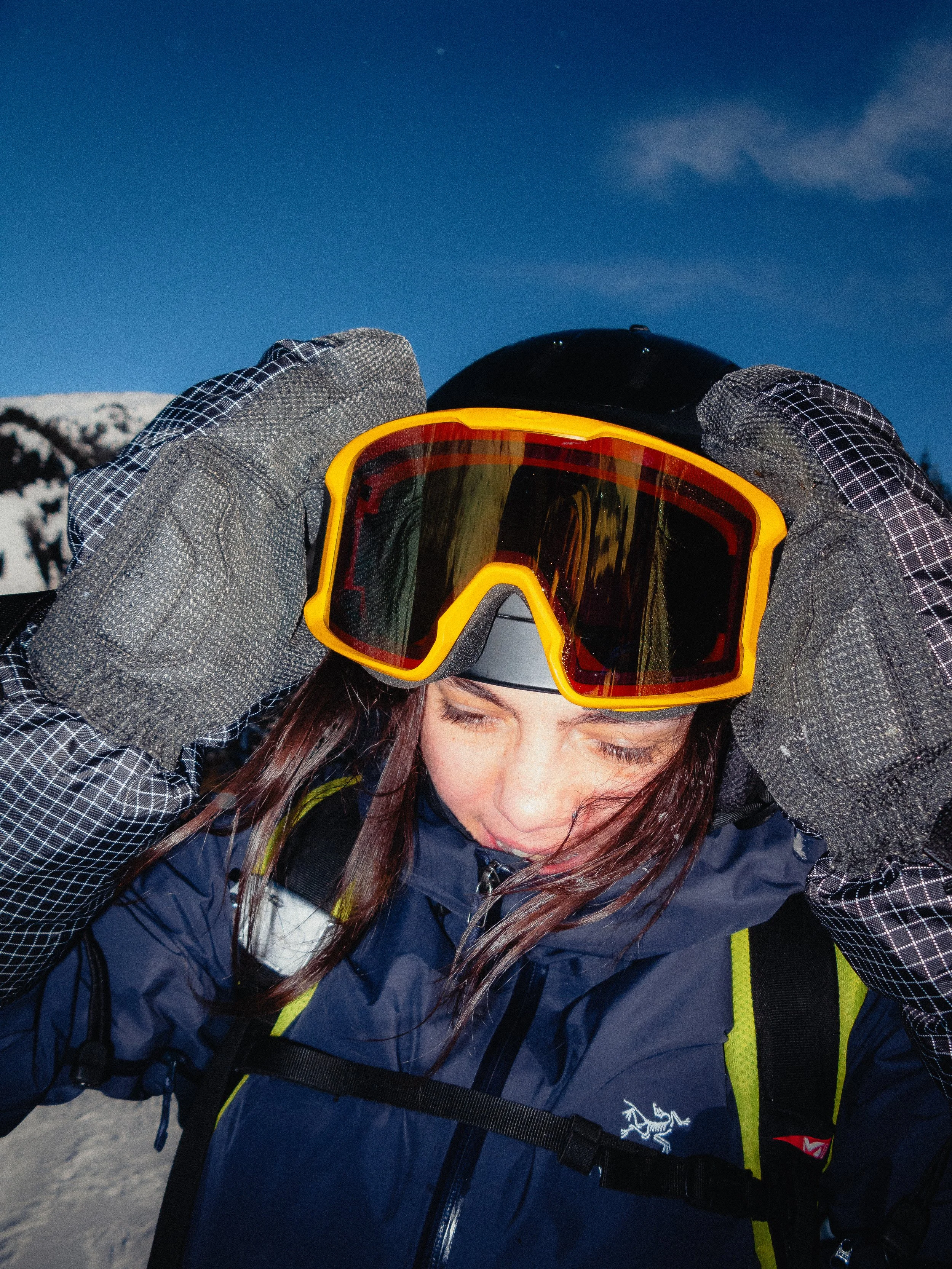 Une personne portant un casque de ski et des lunettes de protection, ajustant l'équipement avec des gants sur une piste enneigée.
