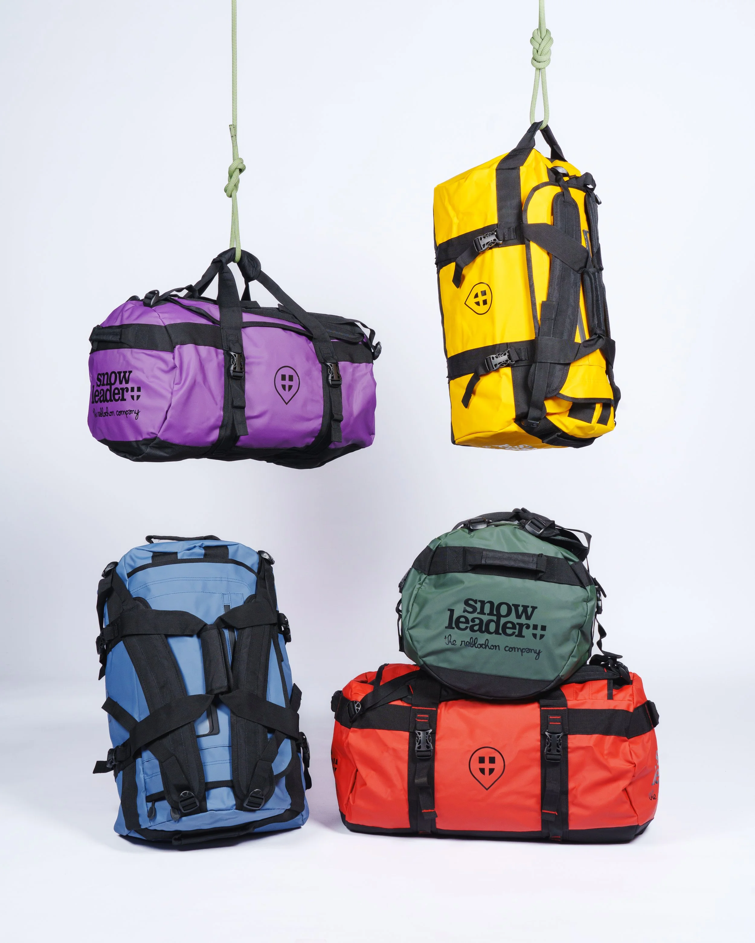 Quatre sacs de sport colorés suspendus, jaune, violet, bleu et rouge, avec le logo "Snowleader" écrit sur certains d'entre eux.