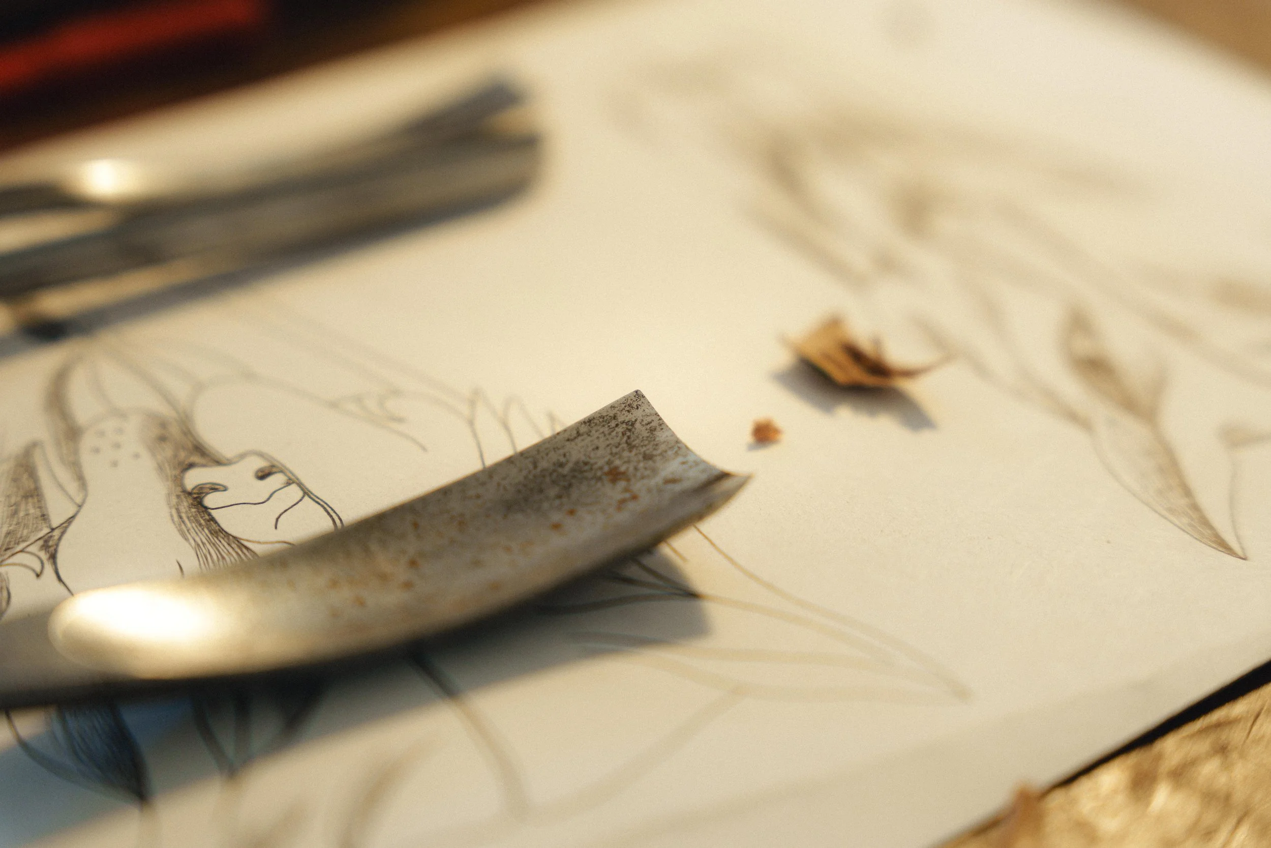 Dessin au crayon sur papier avec outils de gravure en métal dessus, détails de sculpture bois visible.