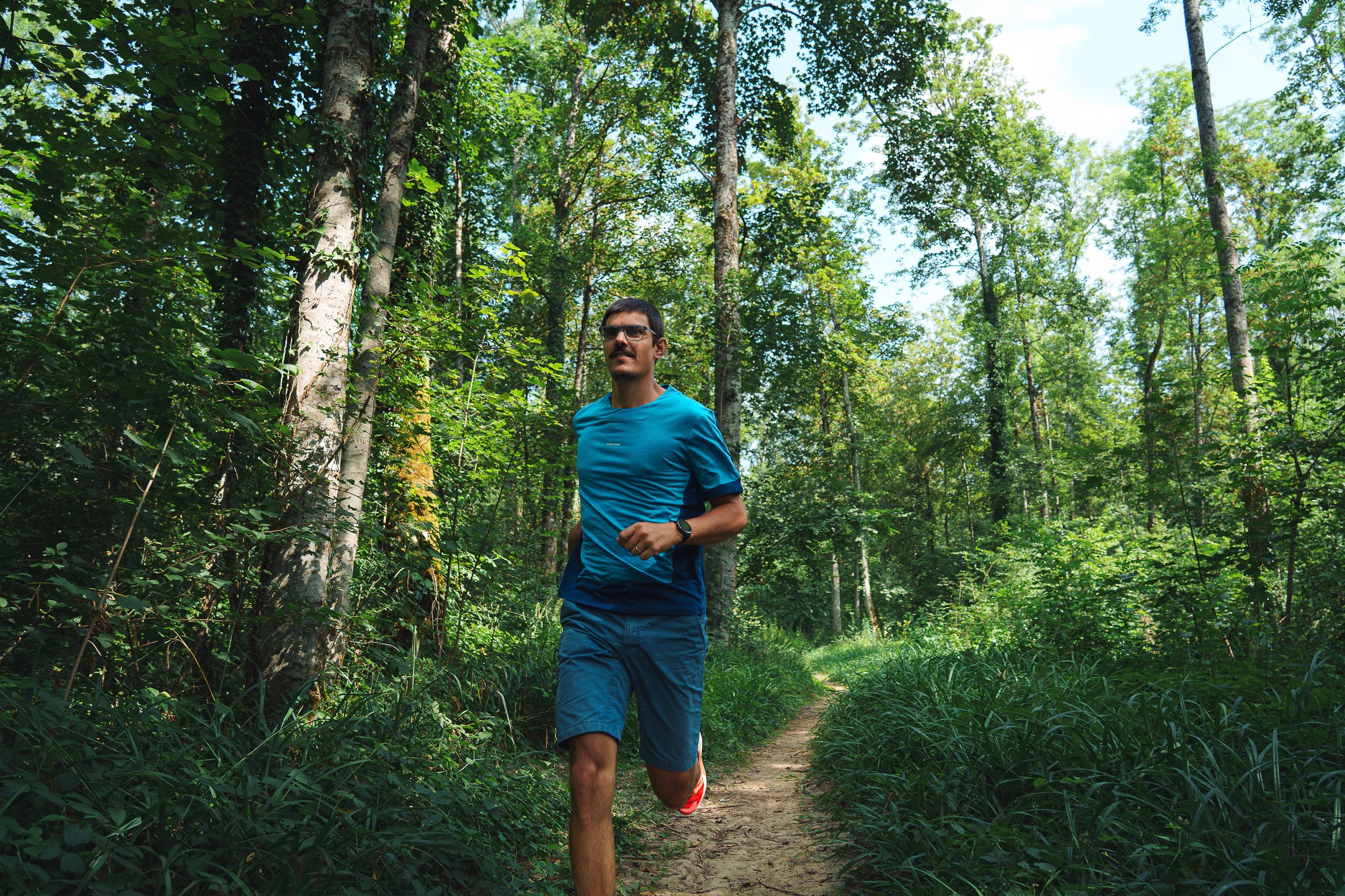 Homme courant sur un sentier en forêt verdoyante.
