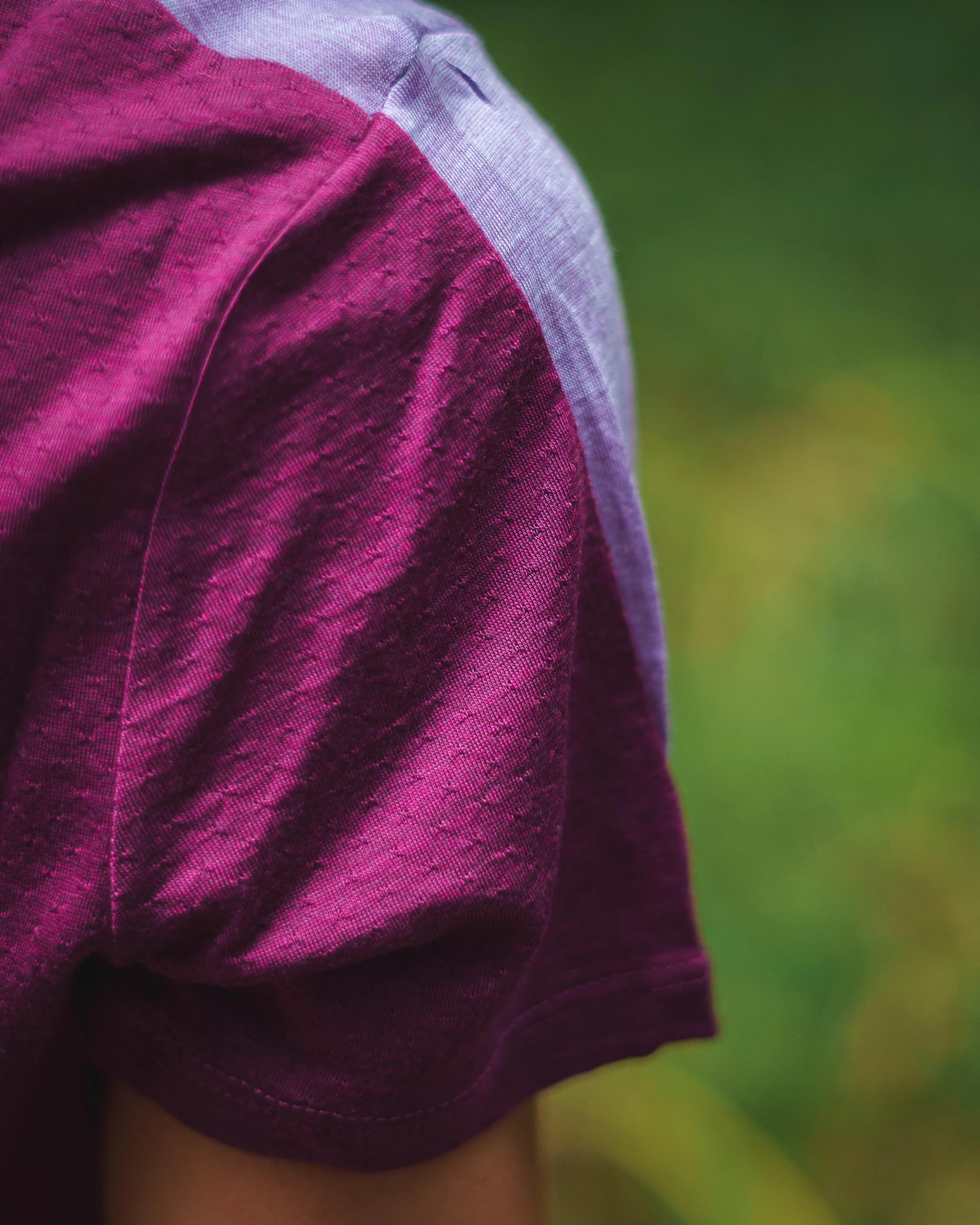 Manche d'un t-shirt violet devant un fond vert flou.