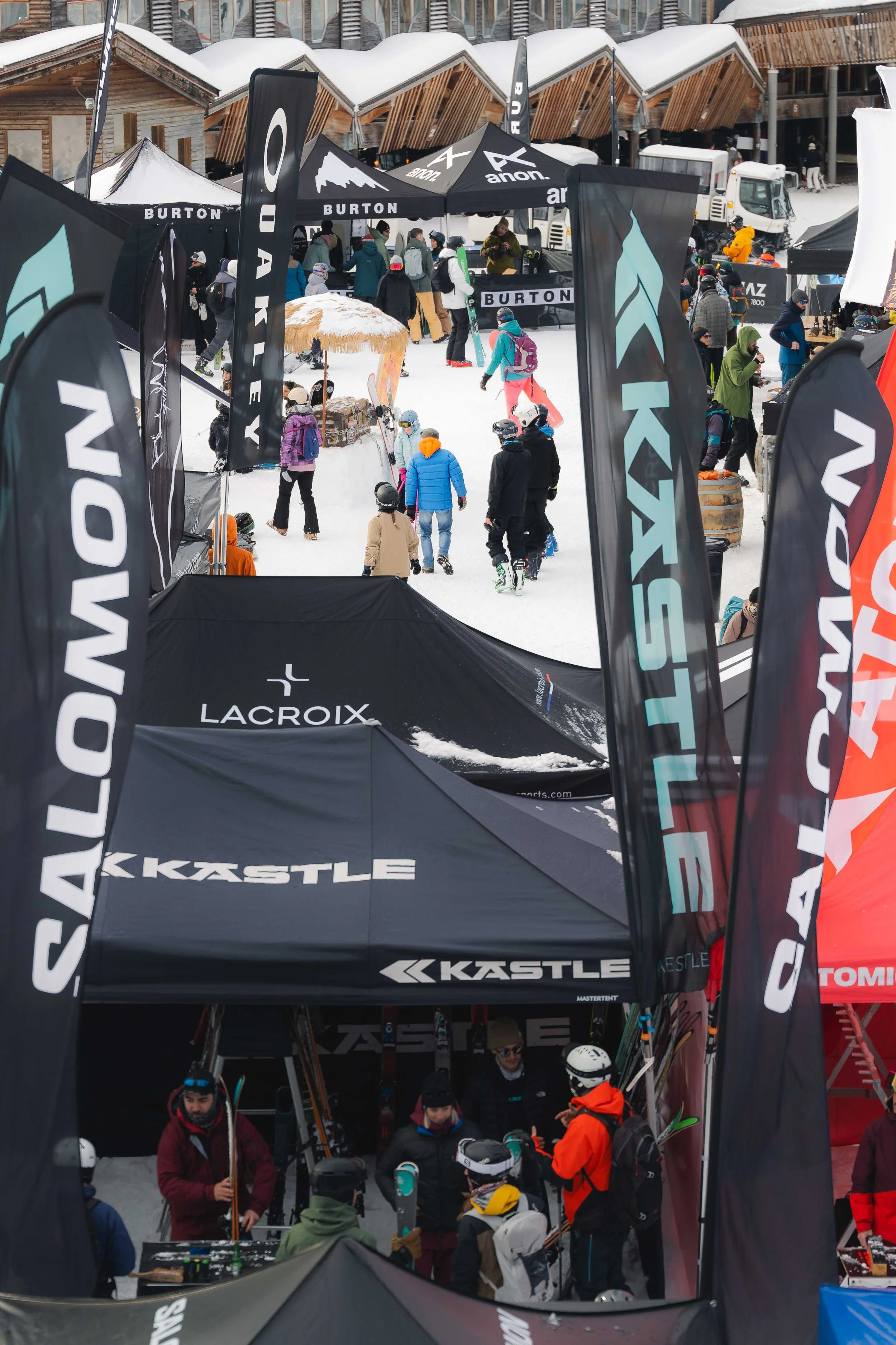 Scène hivernale dans une station de ski avec des tentes de marque et des skieurs.