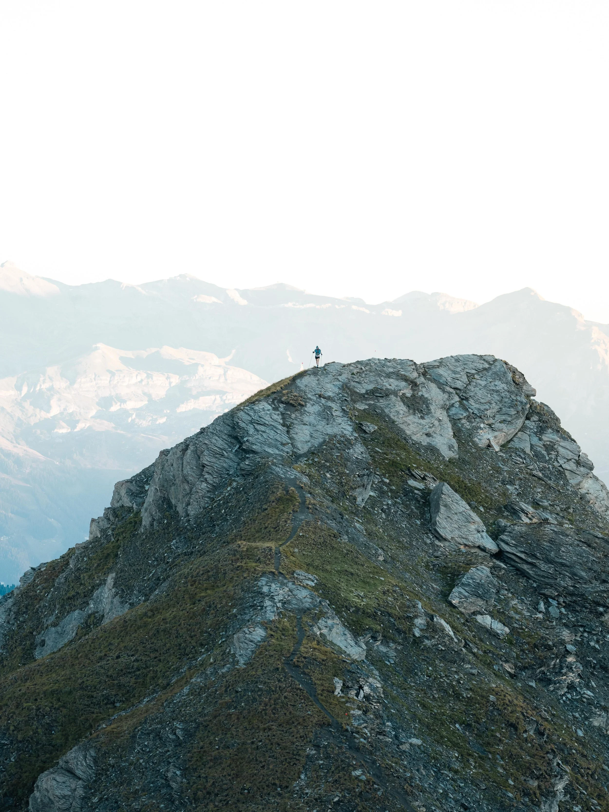 Personne debout au sommet d'une montagne rocheuse avec des montagnes en arrière-plan.