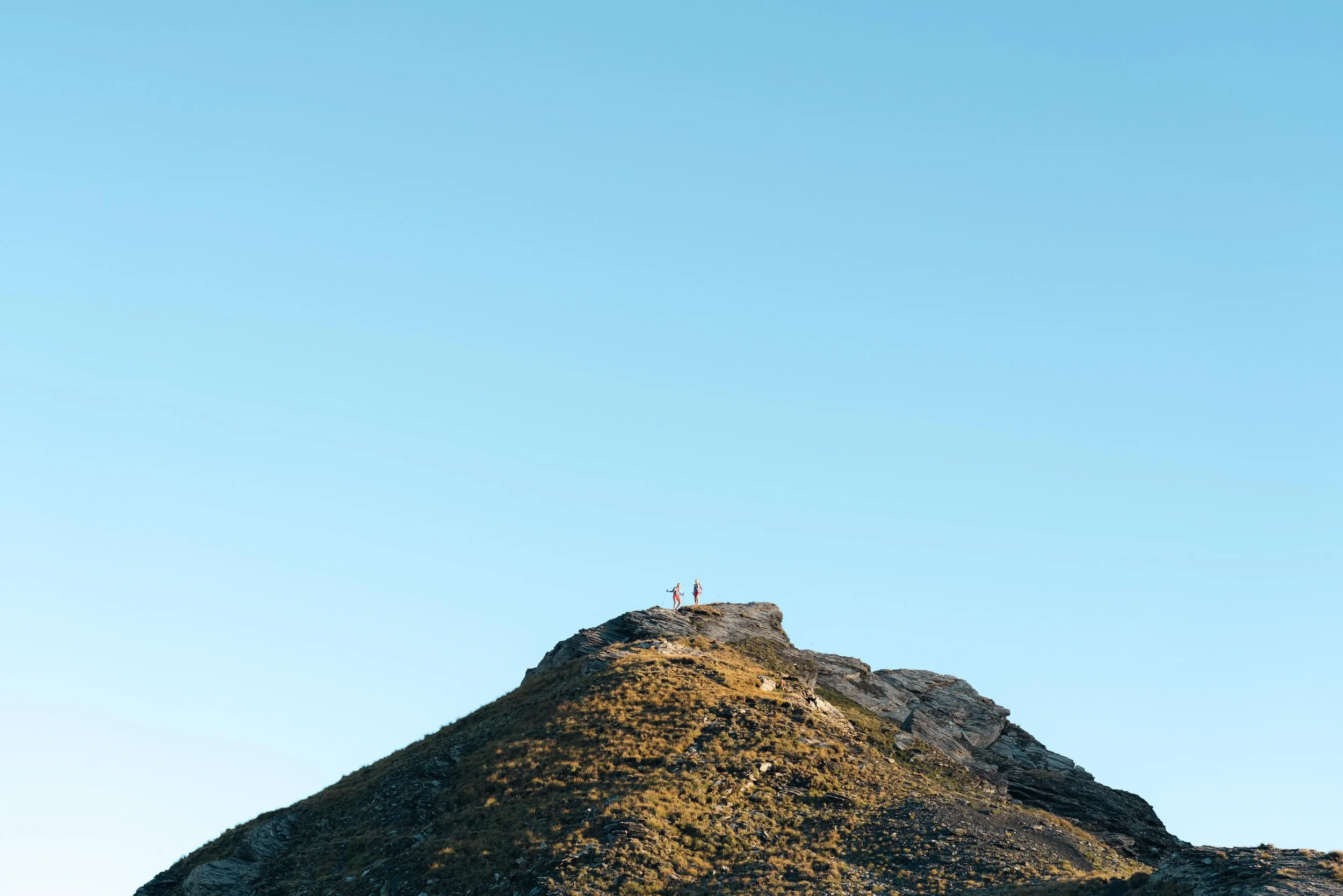 Deux personnes debout au sommet d'une montagne rocheuse sous un ciel bleu clair.
