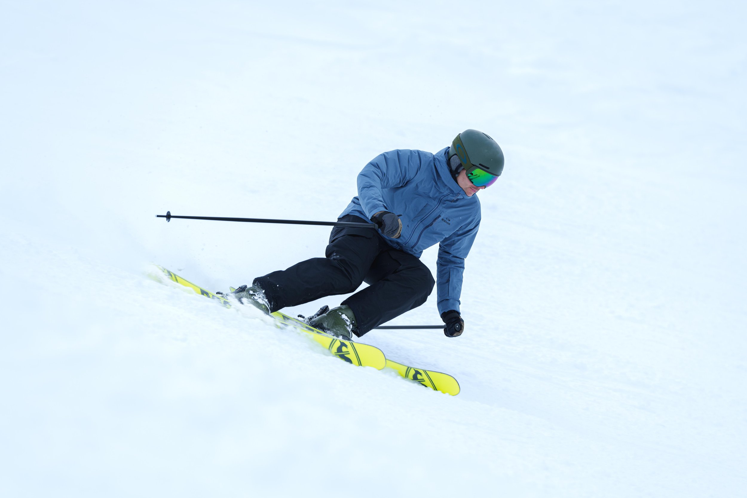 Une personne descendant une pente enneigée en ski, portant une veste bleue et un casque vert.