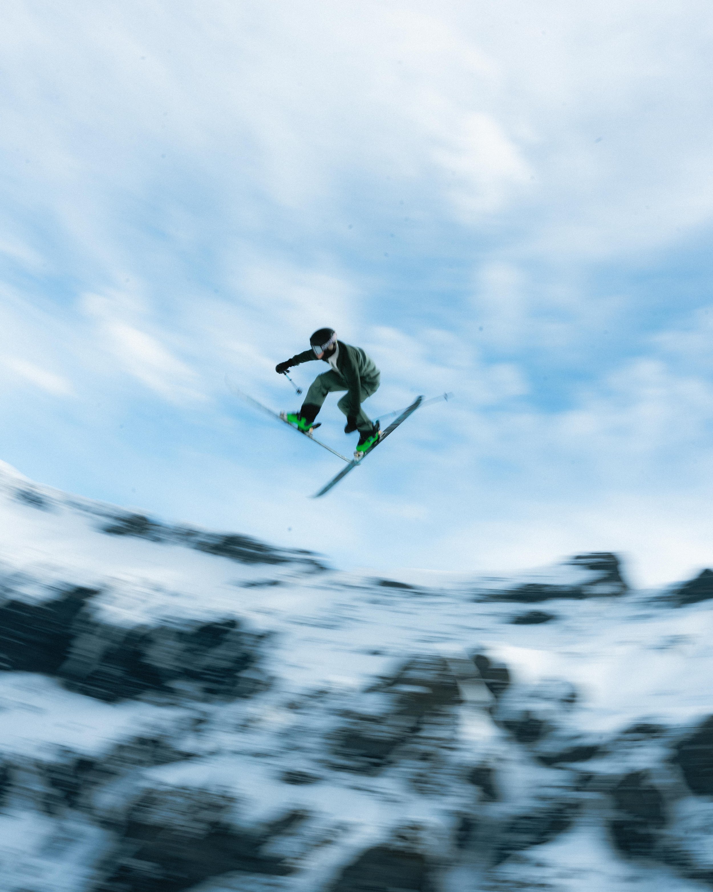 Skieur freestyle en plein saut dans les montagnes enneigées sous un ciel bleu.
