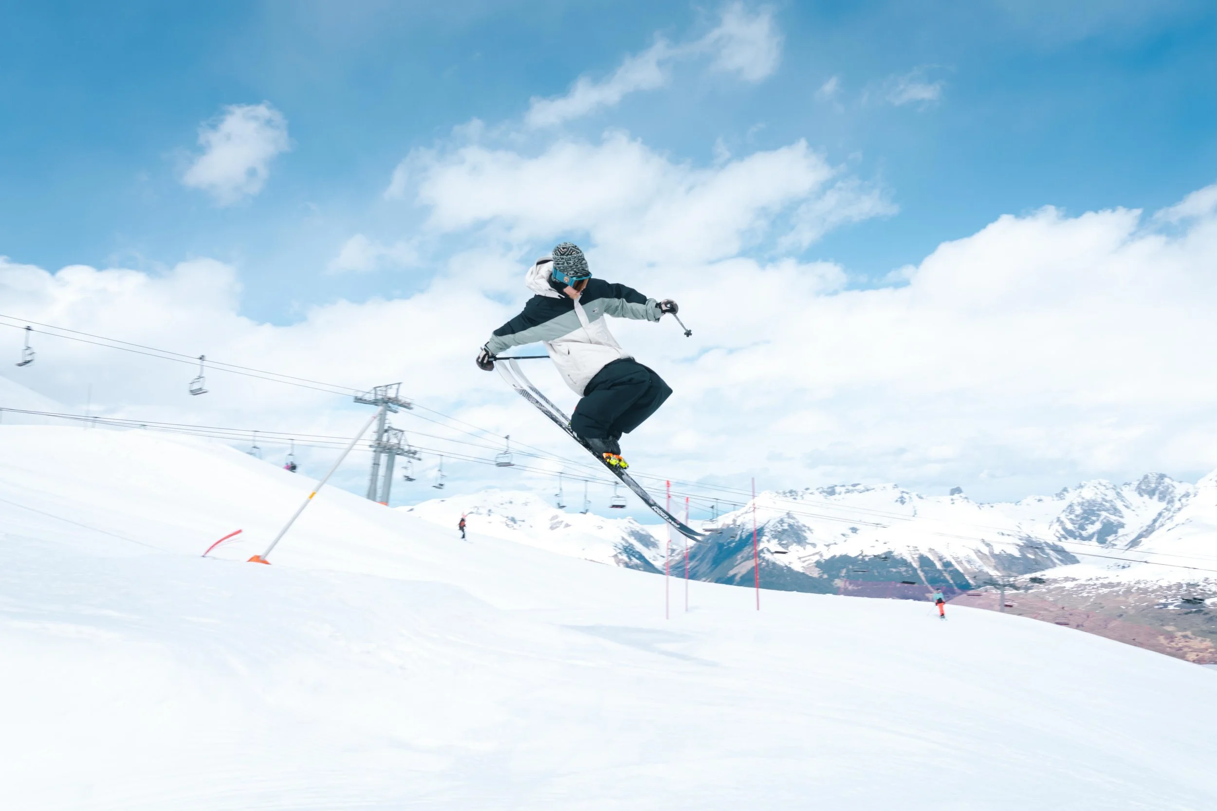 Une personne effectuant un saut en ski sur une piste enneigée avec des montagnes en arrière-plan.