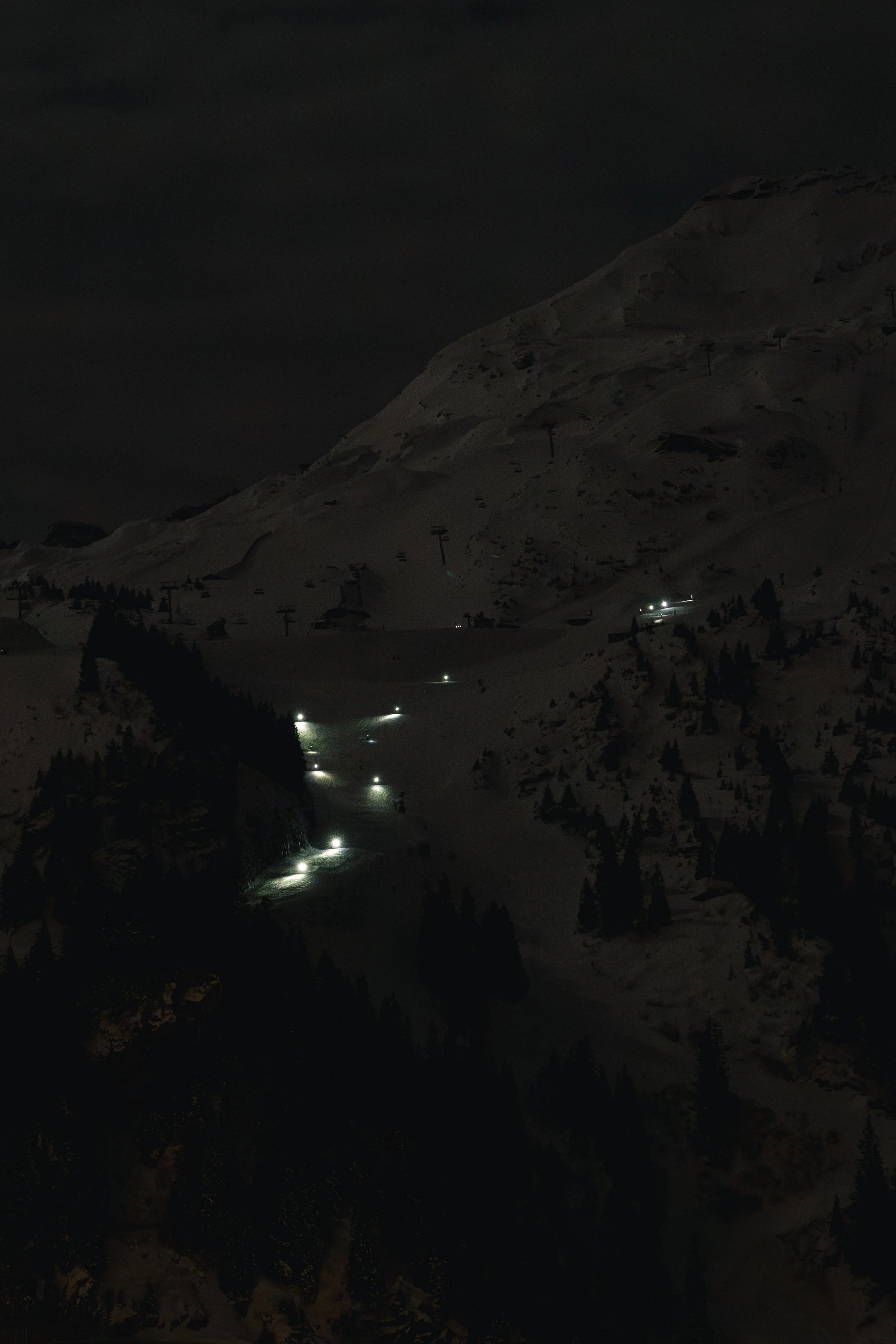 Piste de ski éclairée la nuit dans une montagne enneigée.