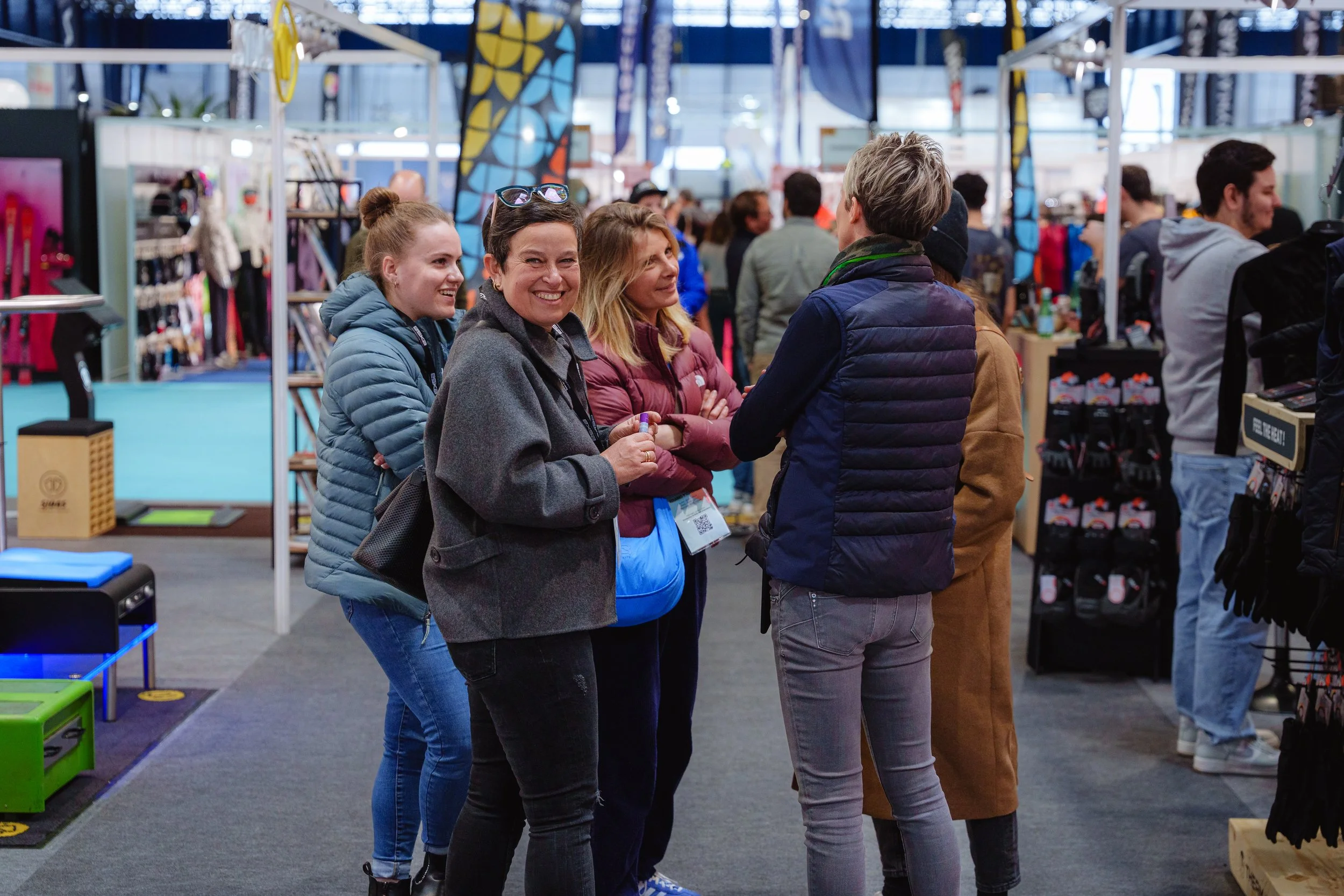 Des personnes souriantes discutant dans un salon professionnel avec des stands et des vêtements exposés.
