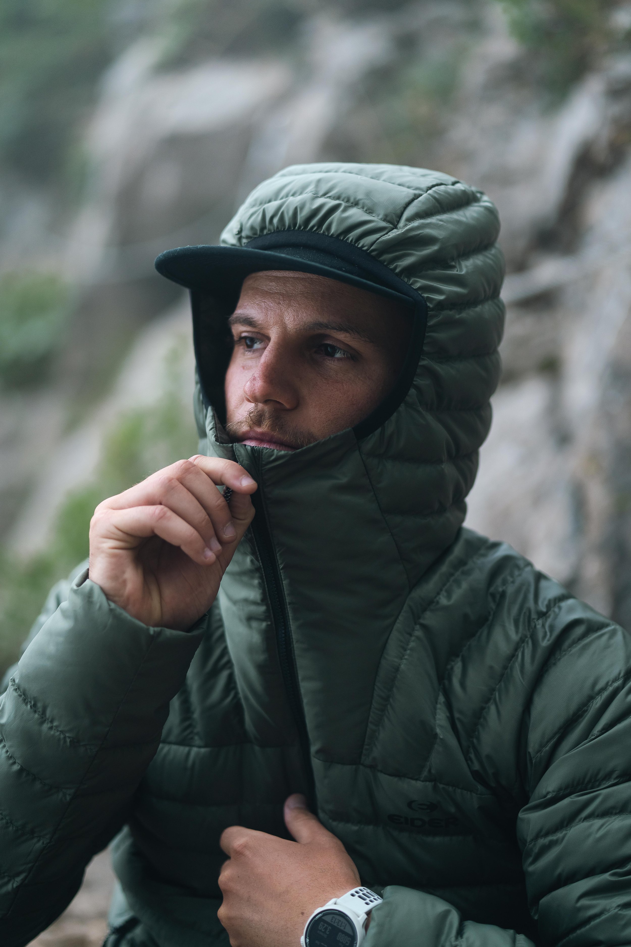 Personne portant une veste matelassée verte avec une capuche, extérieurs flous en arrière-plan.