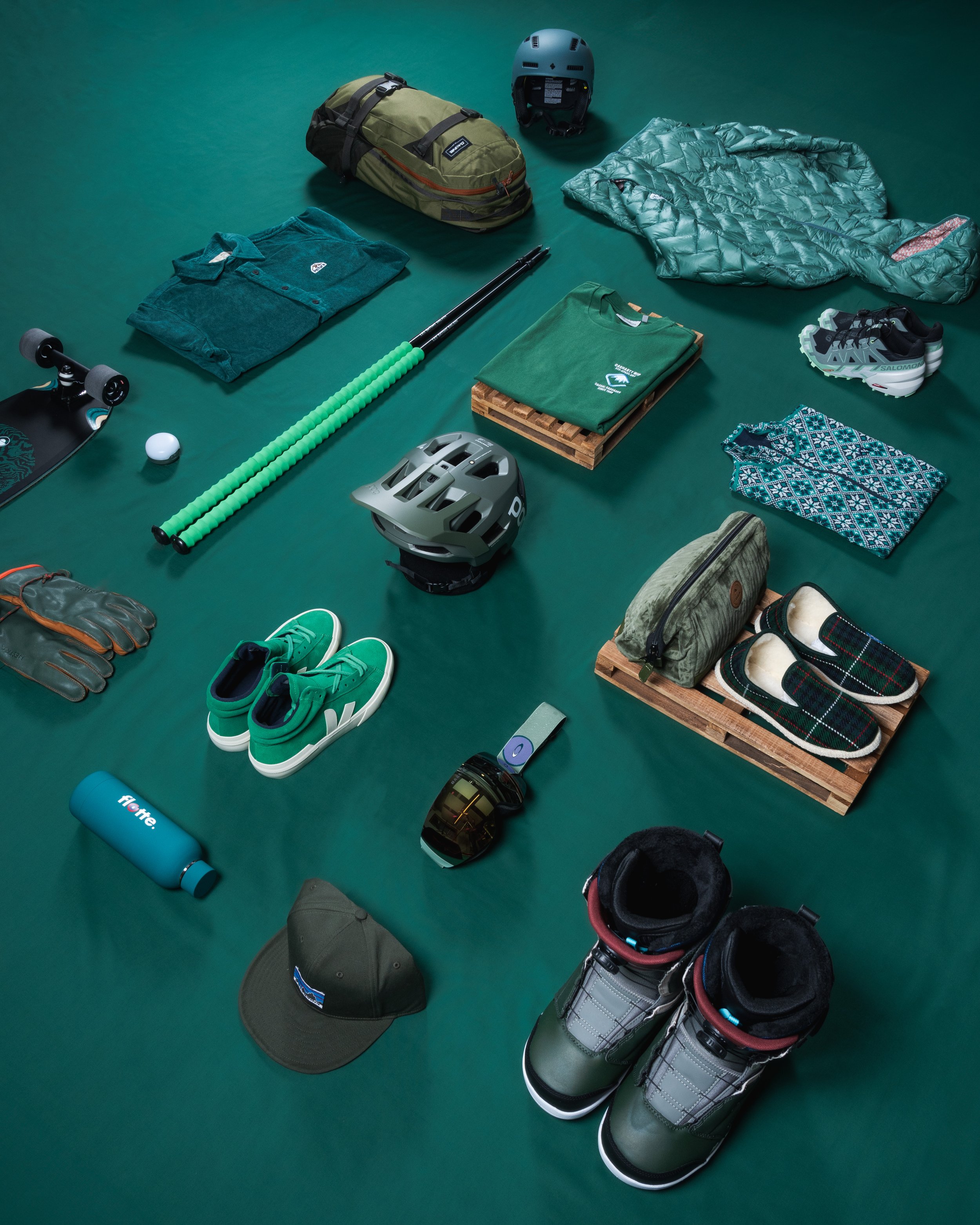 Divers articles de sport et vêtements verts disposés sur un fond vert, incluant un sac à dos, des chaussures, un pull, des gants, des pantalons, un casque, une gourde, et une casquette.