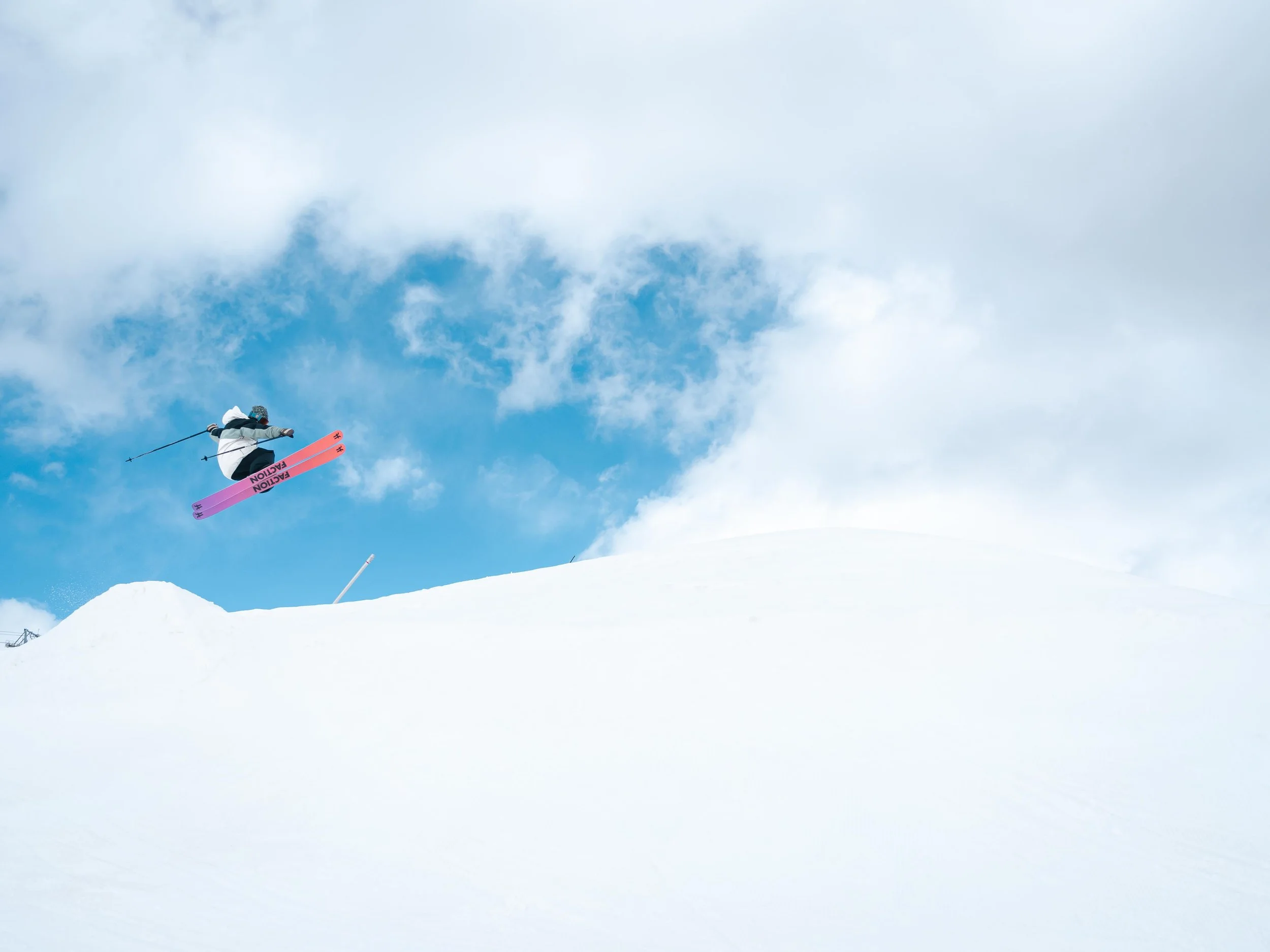 Un skieur effectuant un saut acrobatique dans un paysage enneigé avec un ciel bleu en arrière-plan.