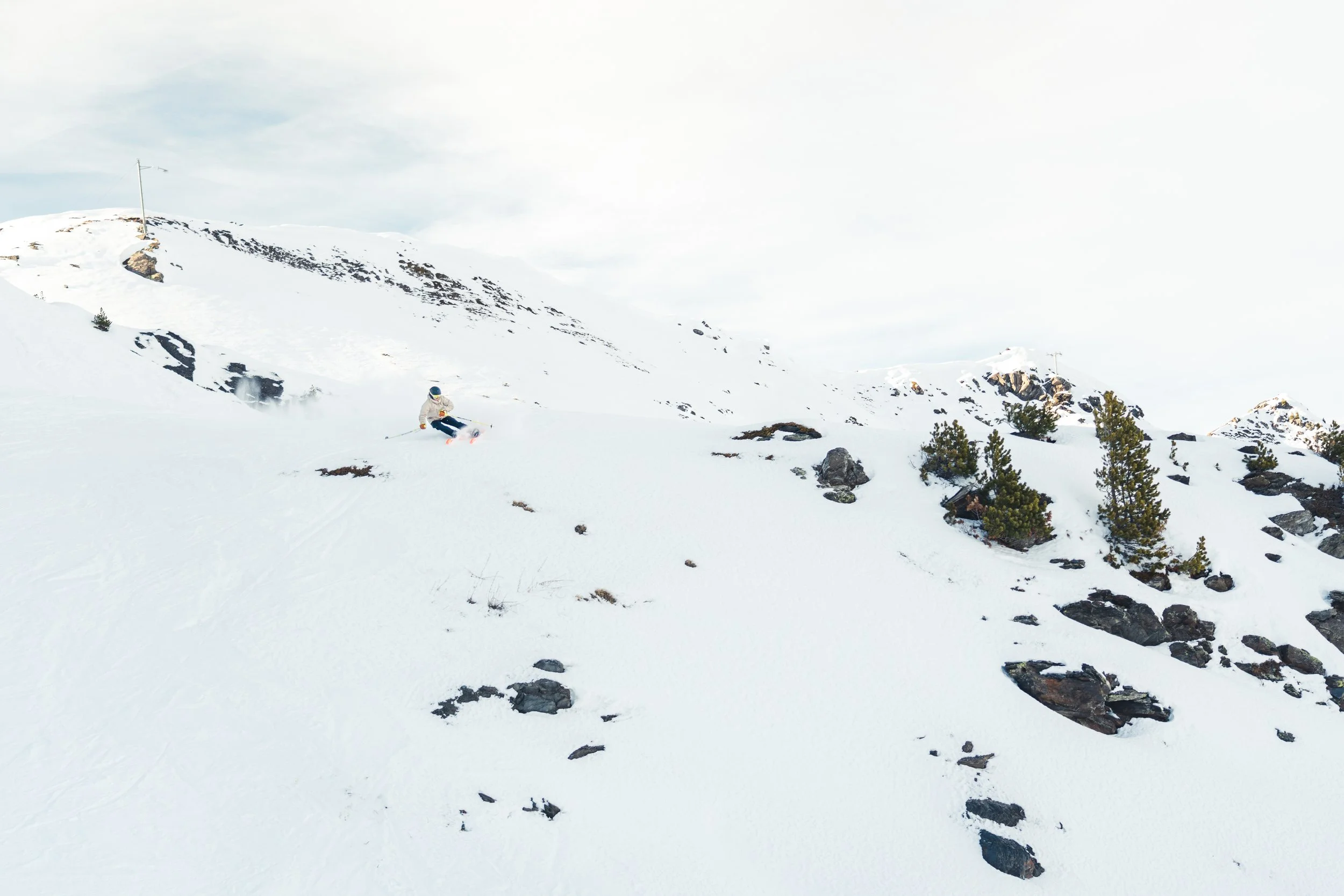 Un paysage de montagne enneigé avec un skieur descendant la pente, des arbres et des rochers dispersés sur la neige.
