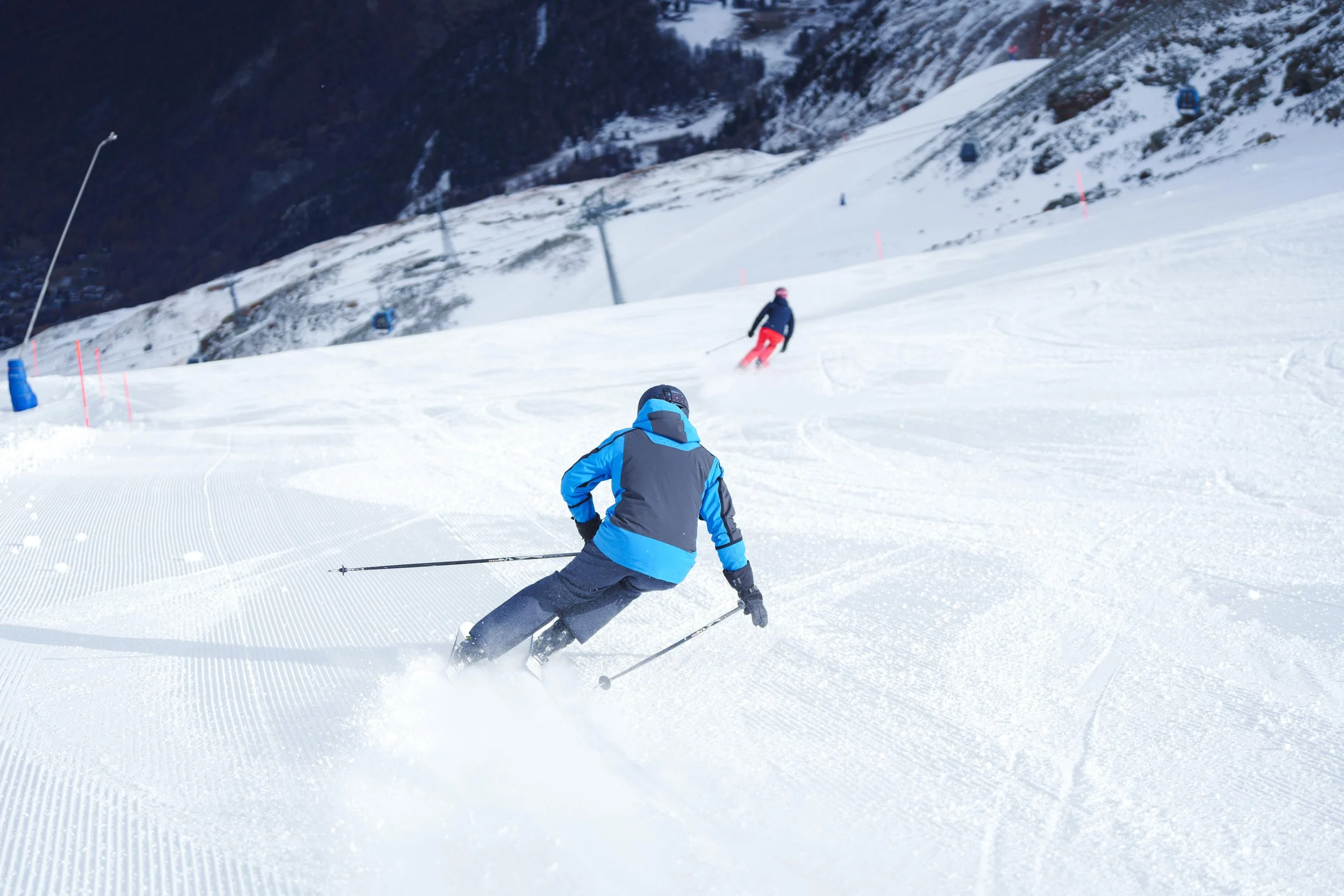 Deux skieurs descendant une piste enneigée, l'un portant une veste bleue.
