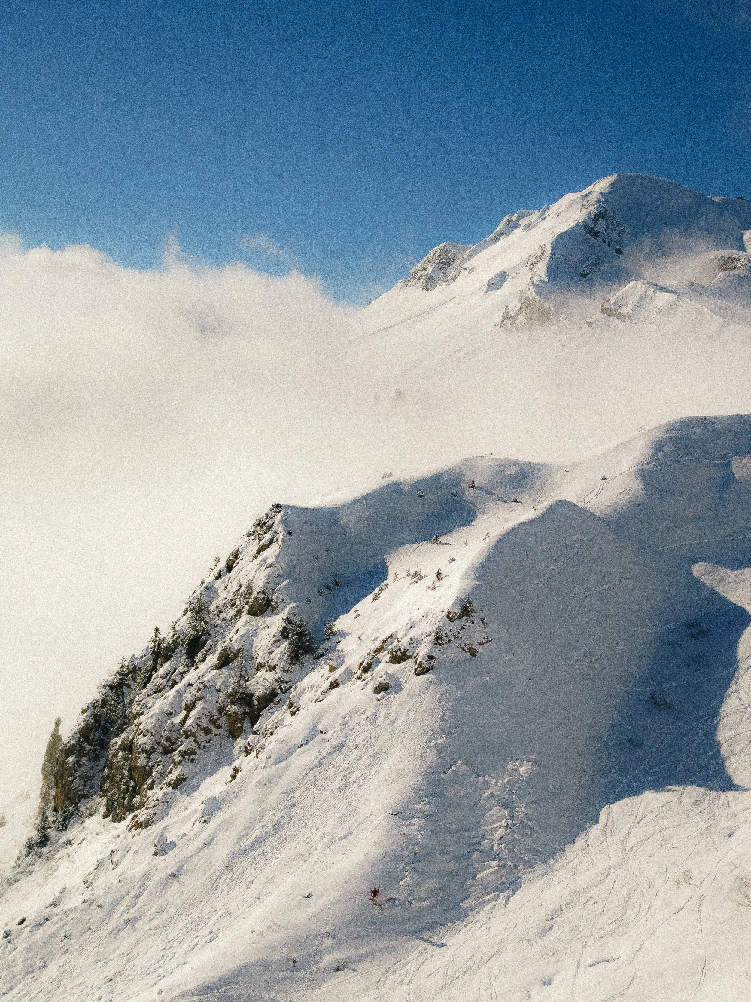 Paysage de montagne enneigée avec un ciel bleu et des nuages, vue sur des pentes de ski.