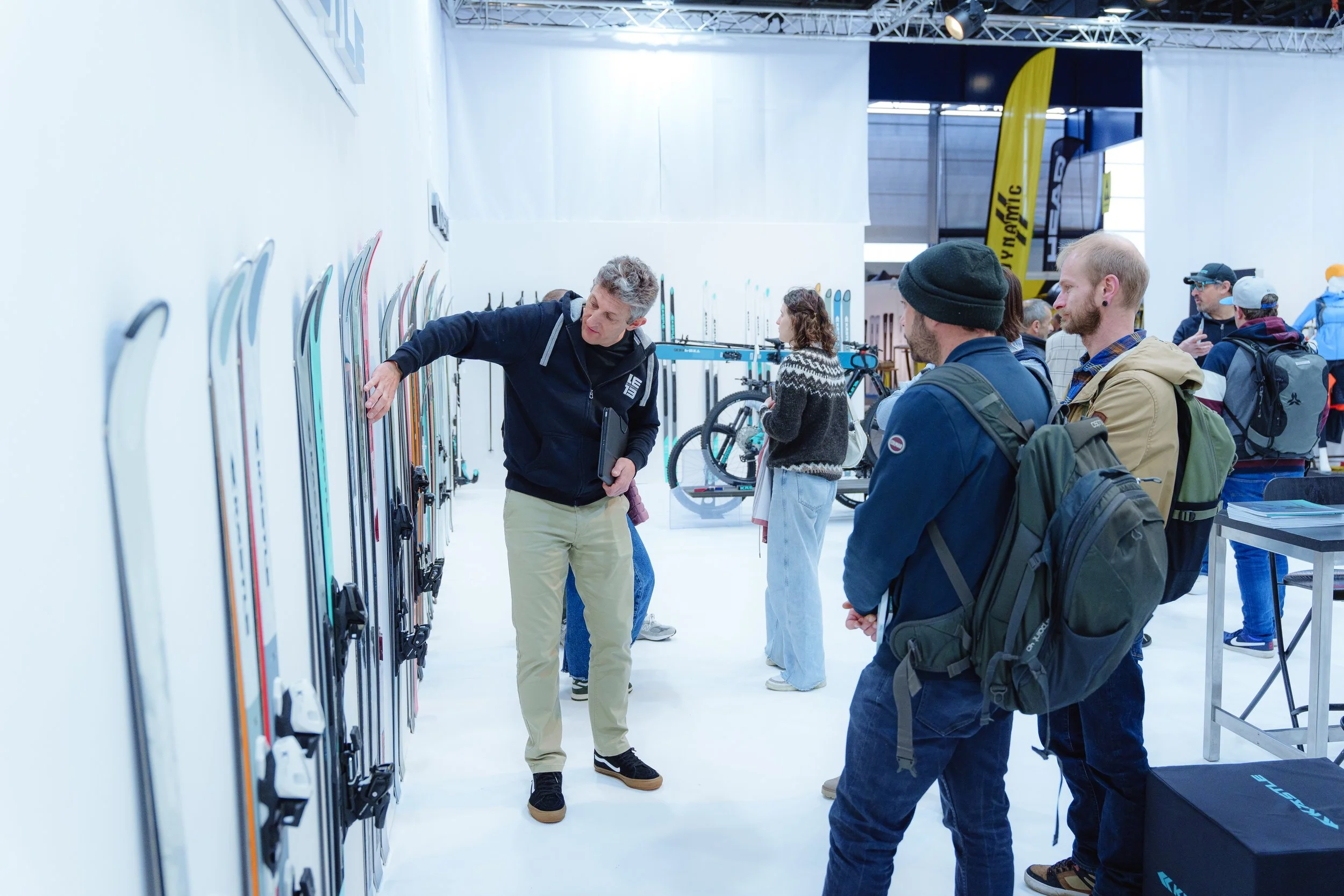 Un homme montre des skis à un groupe de personnes dans un salon professionnel.