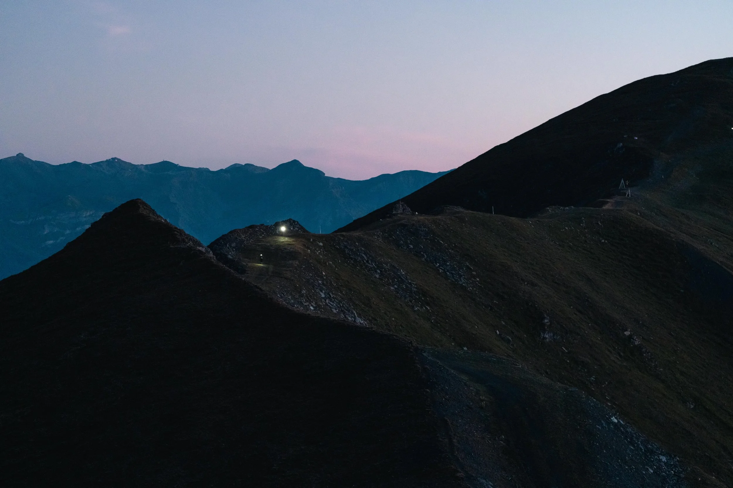 Paysage montagneux au crépuscule avec une lumière sur un sentier.