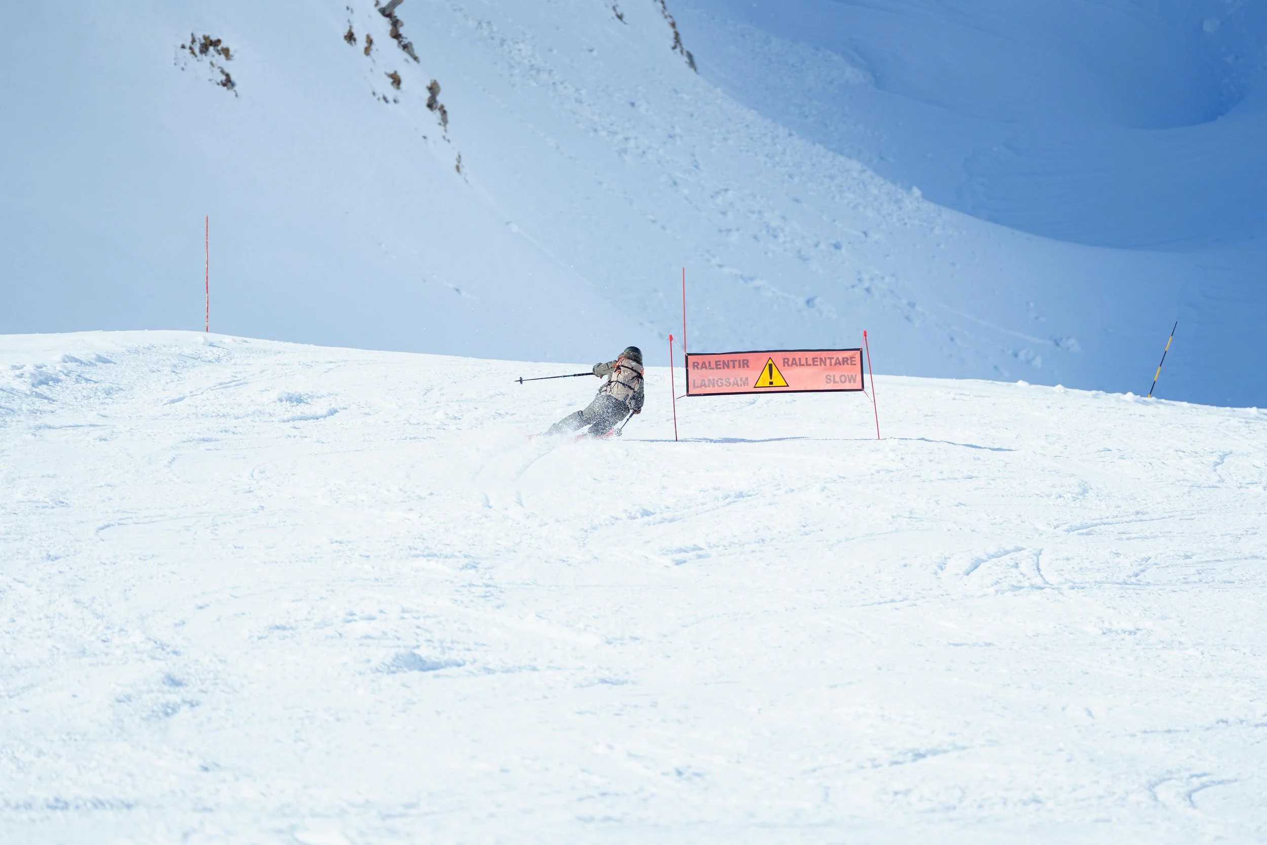 Skieur sur une piste enneigée avec un panneau de signalisation 'Ralentir' à l'arrière-plan."