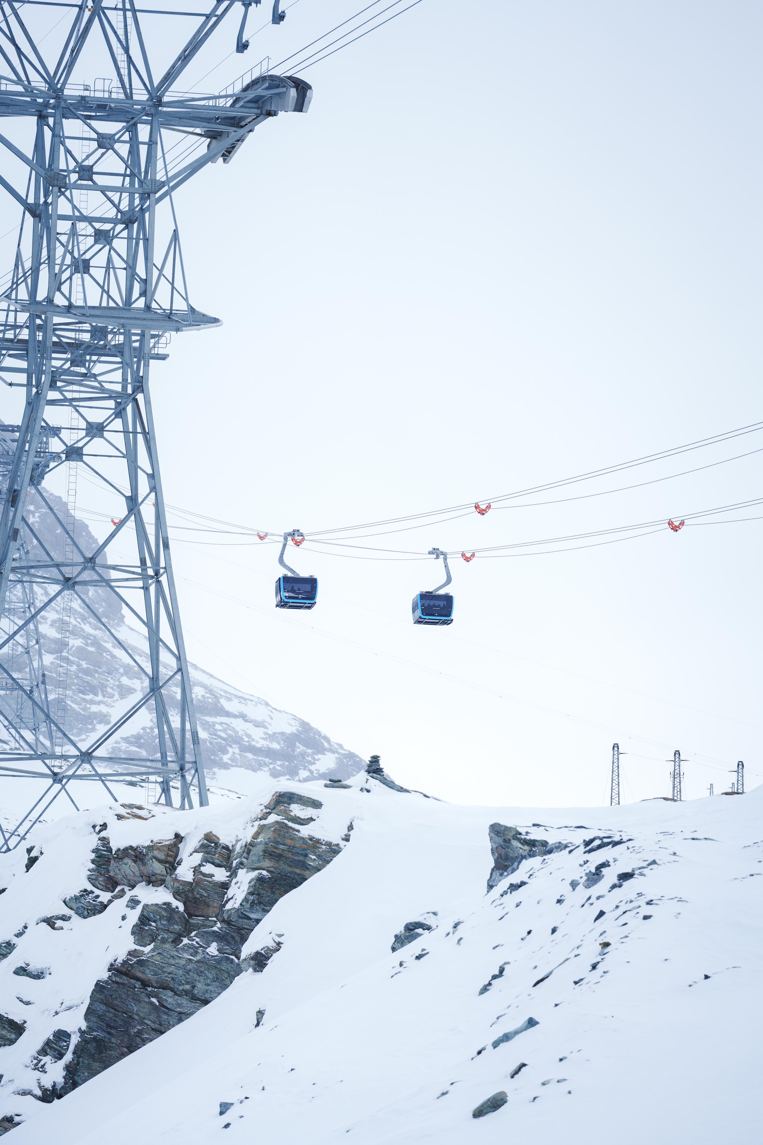 Téléphériques suspendus au-dessus d'un paysage enneigé avec pylones métalliques et montagnes en arrière-plan.