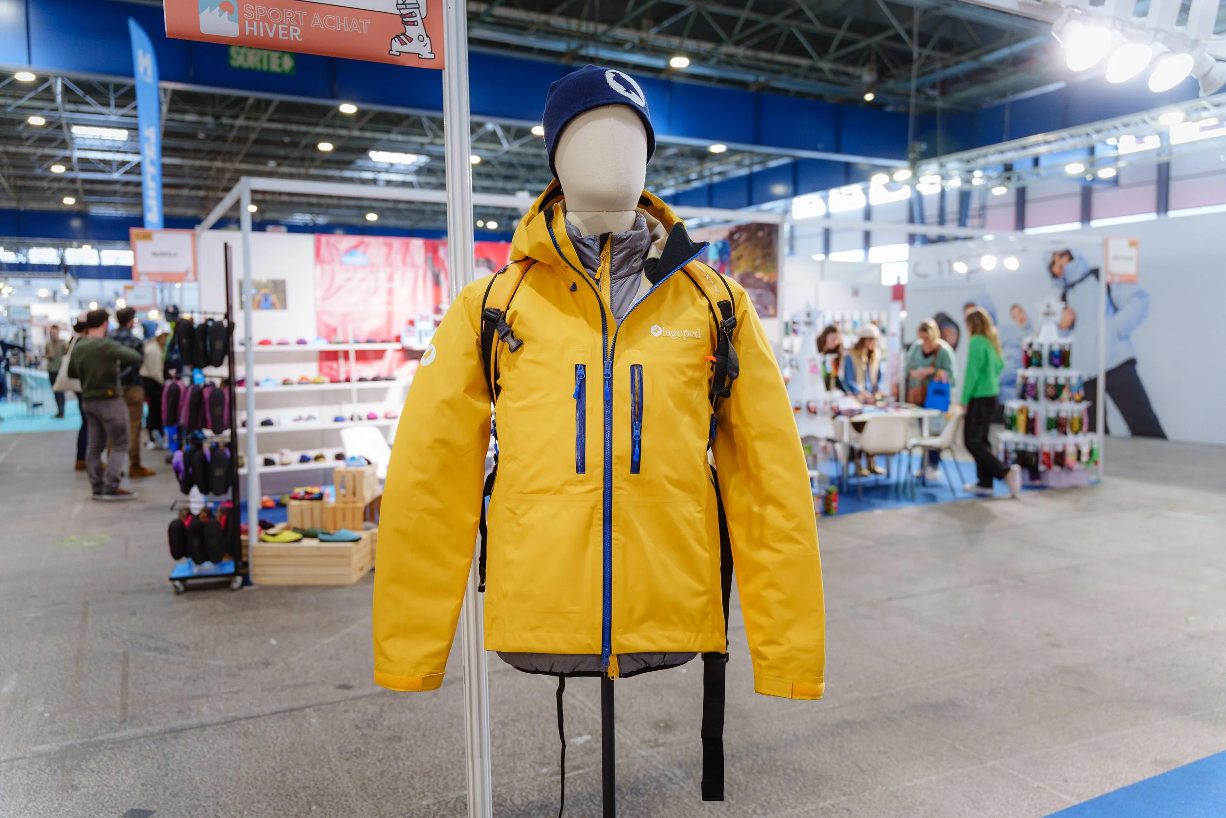 Mannequin avec veste jaune et bonnet, stand d'exposition de vêtements d'hiver en arrière-plan.