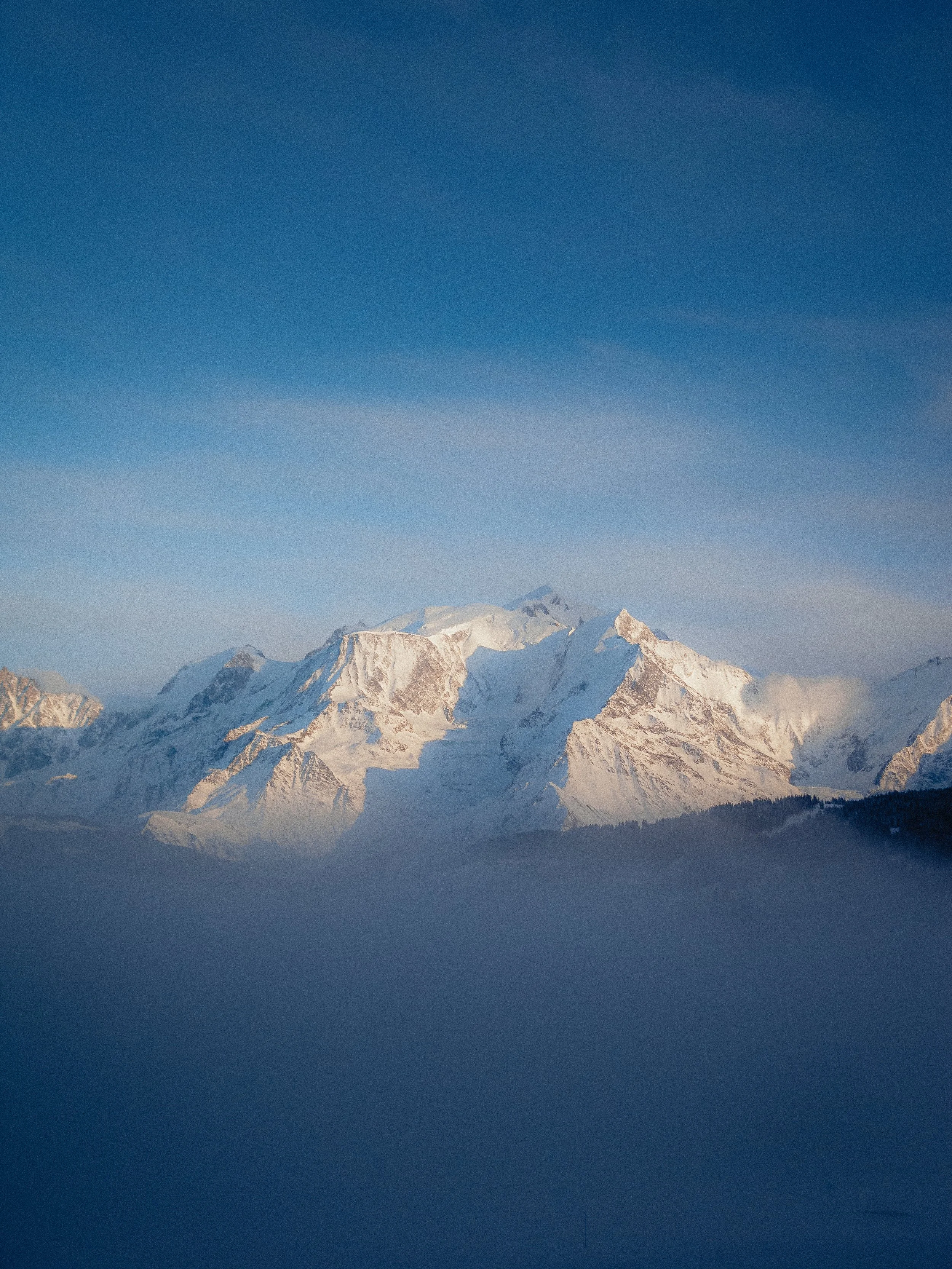 Des montagnes enneigées sous un ciel bleu avec un peu de brouillard à leur base.