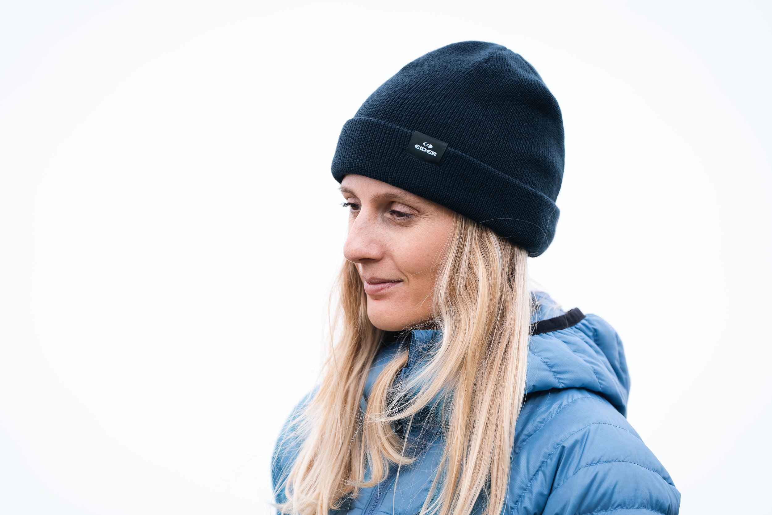 Femme blonde portant un bonnet noir et une veste bleue.