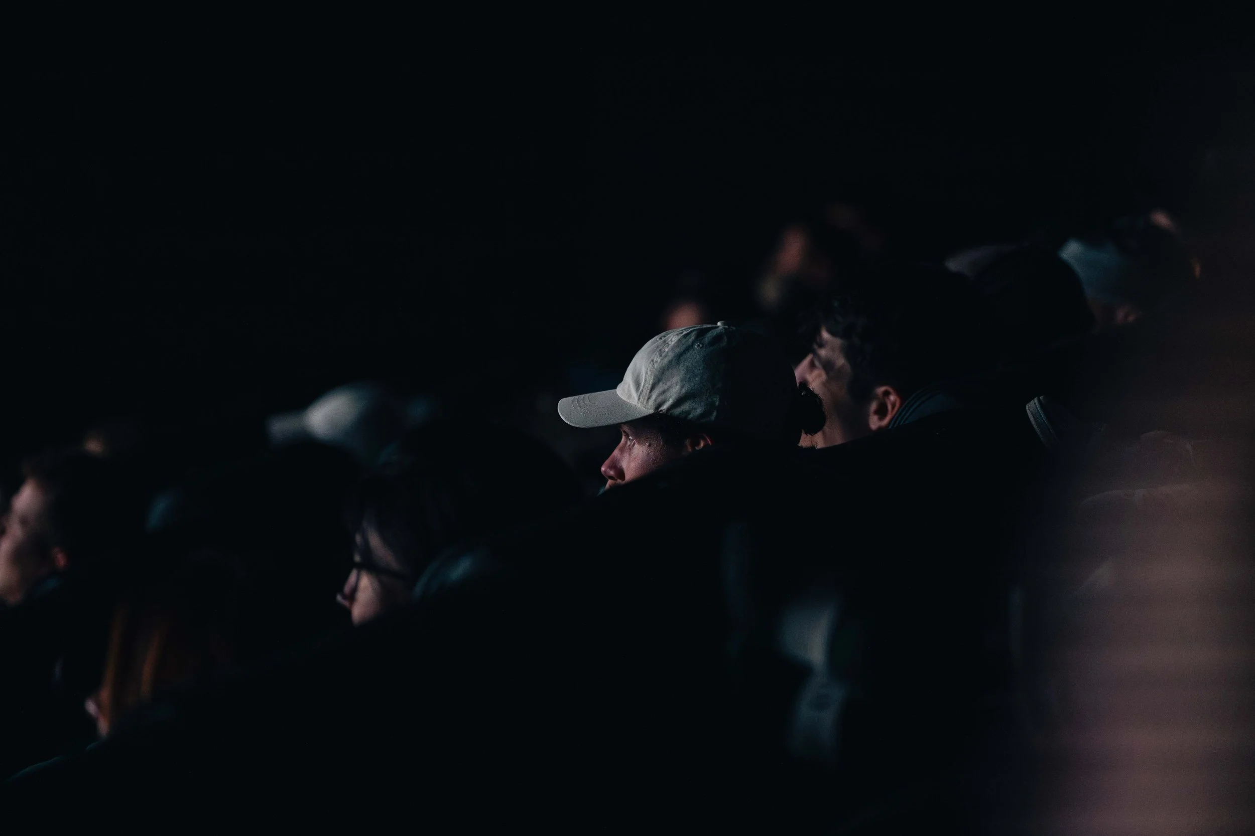 Spectateurs dans une salle de cinéma sombre, certains portant des casquettes.